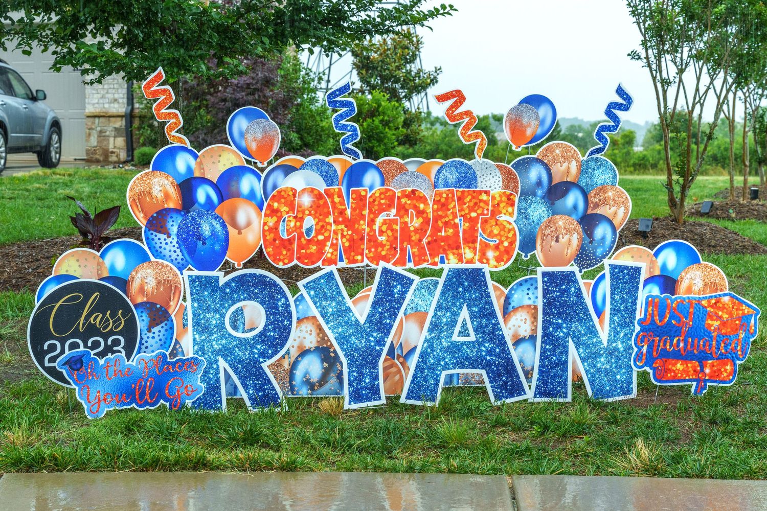 Blue and orange graduation yard sign reading Congrats Ryan with Class of 2023 balloons and streamers.