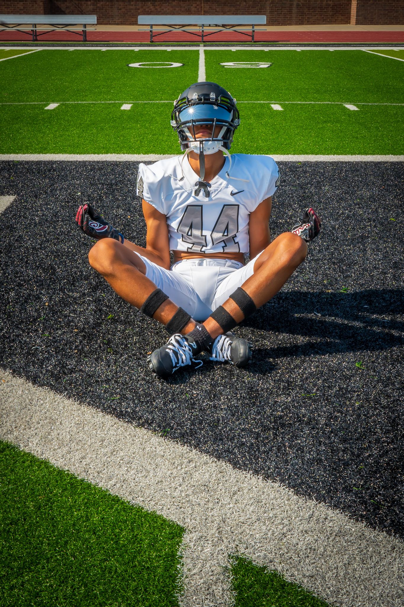 Football player wearing number 44 sits cross-legged meditating on field in white uniform and helmet.