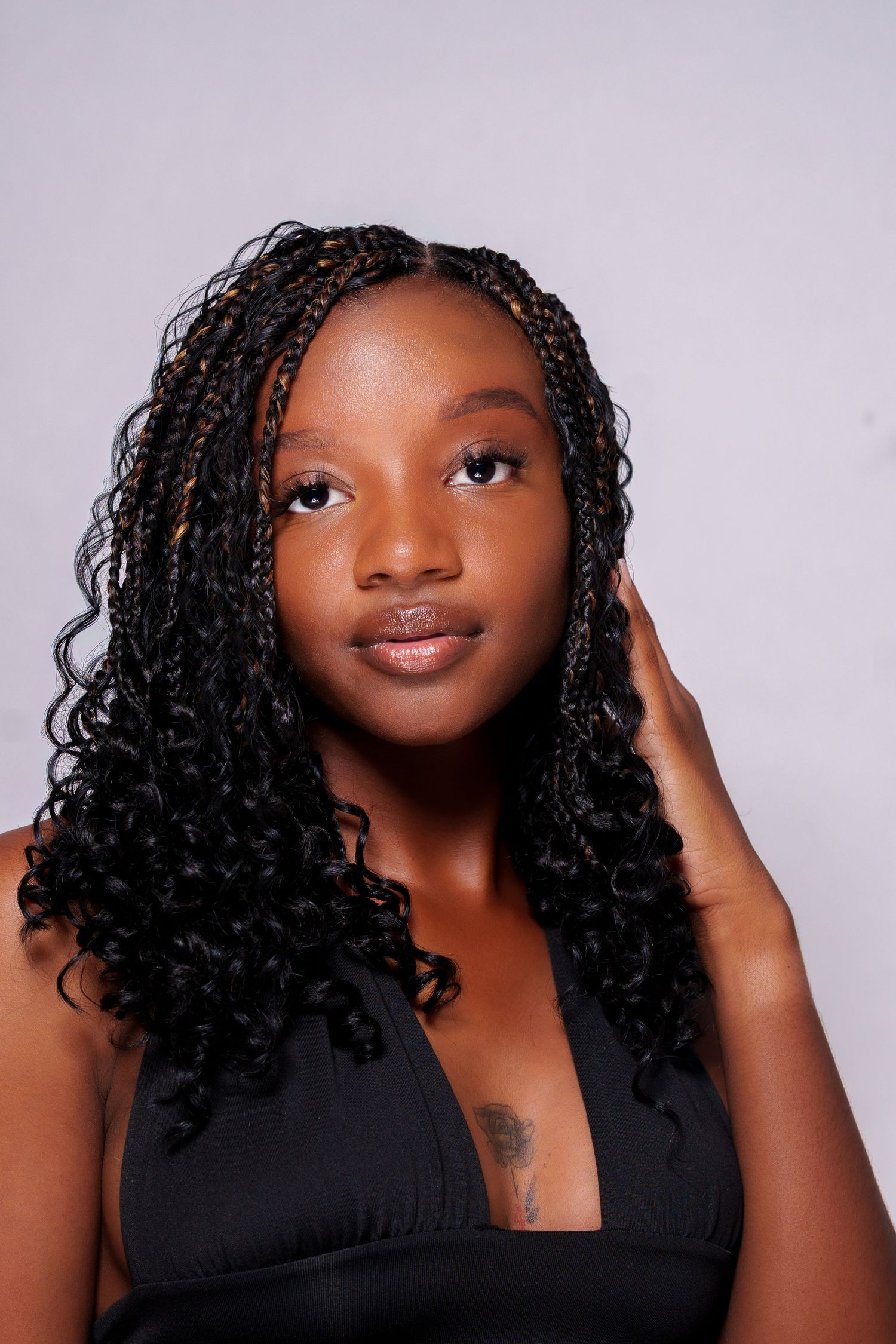 Beautiful young woman with long box braids and curly ends poses in a black halter top.