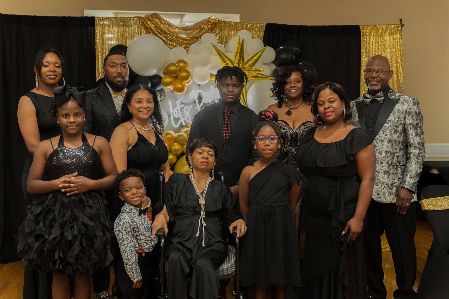 Large family group in black formal attire posing at a celebration with gold star balloon decor.