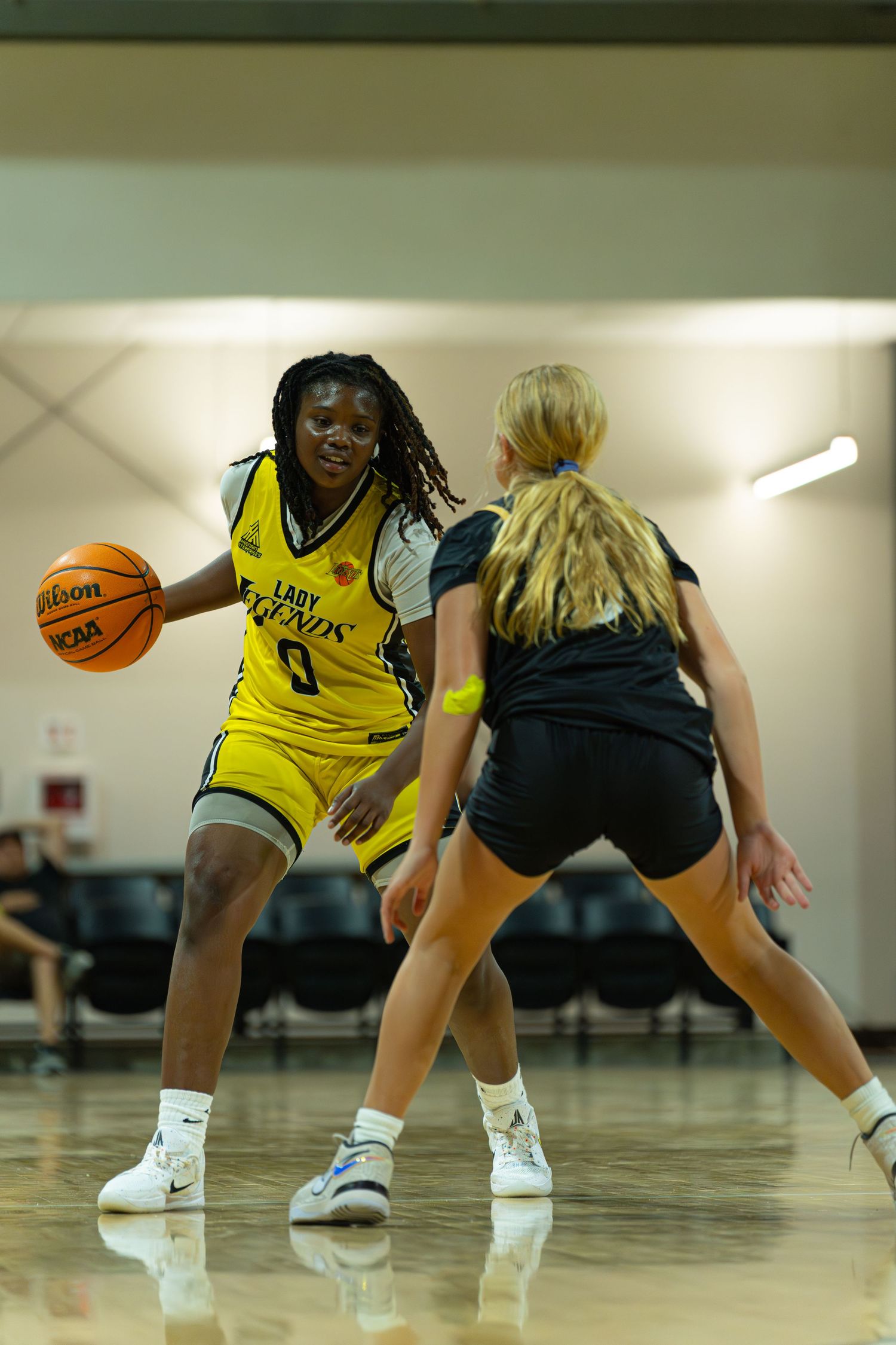 Lady Phenix #3 female basketball player dribbles against defender during indoor basketball game.