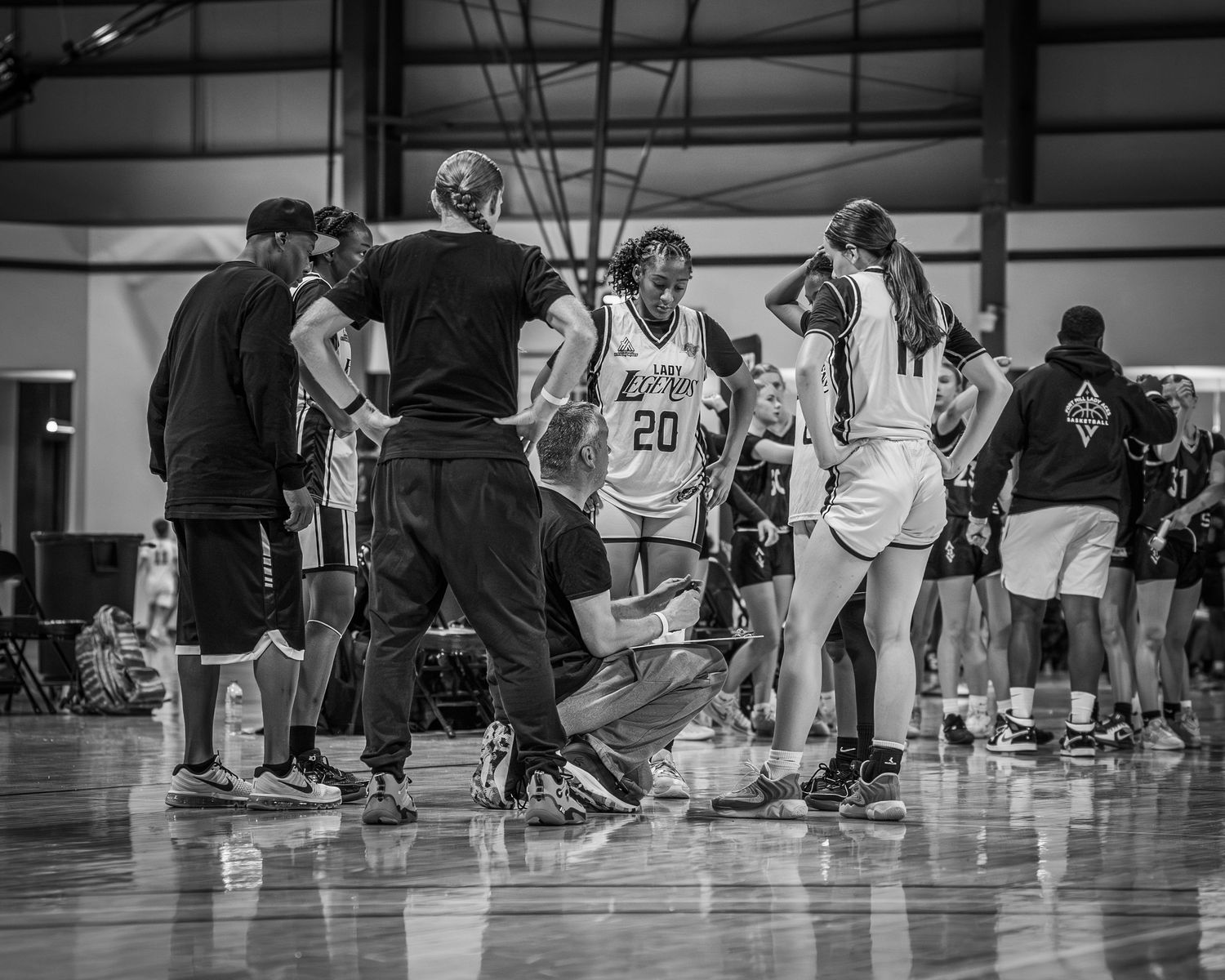 Black and white photo of a women's basketball team huddle during a game timeout on an indoor court.
