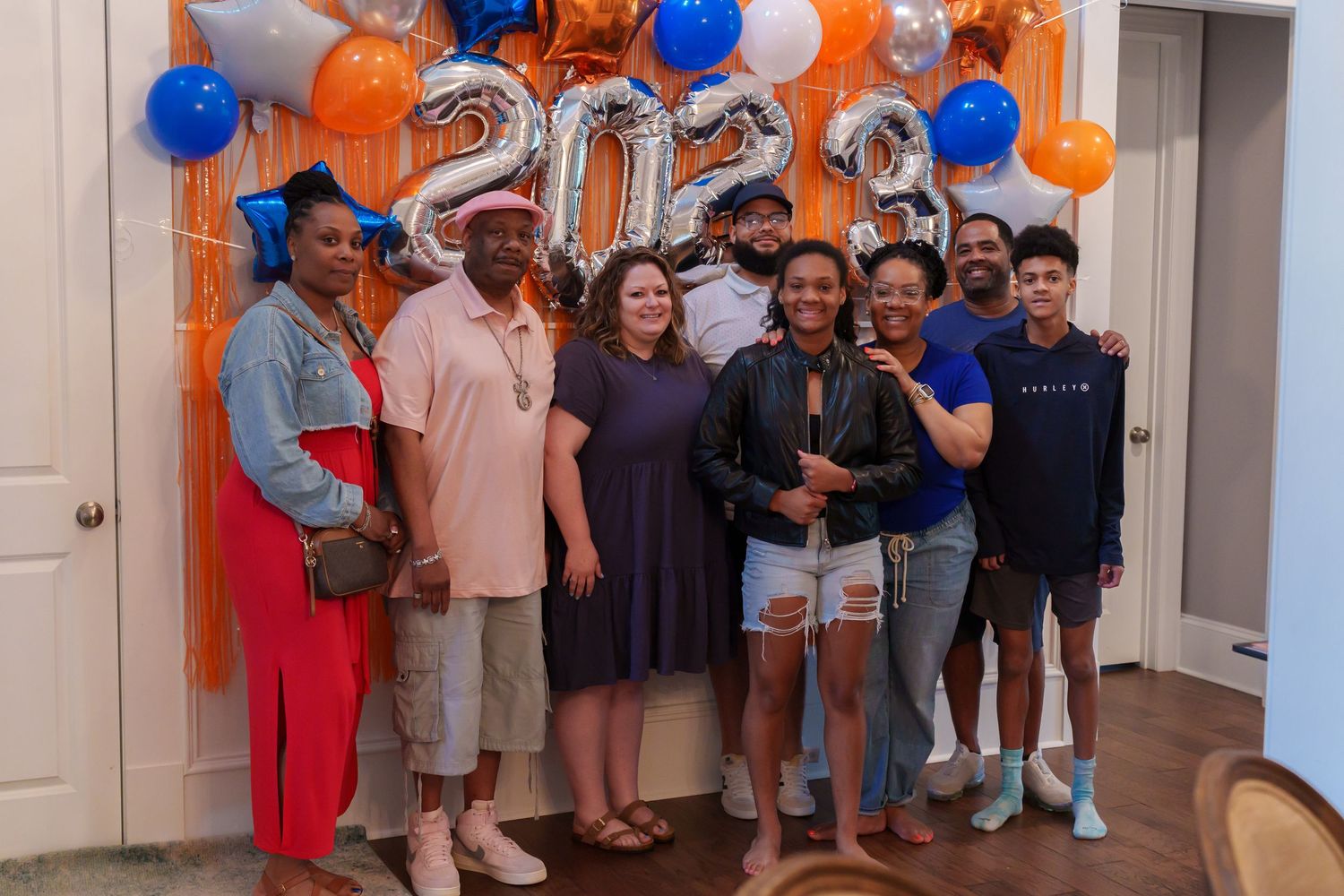 Group of eight people posing together in front of 2023 balloon decorations at a graduation party.