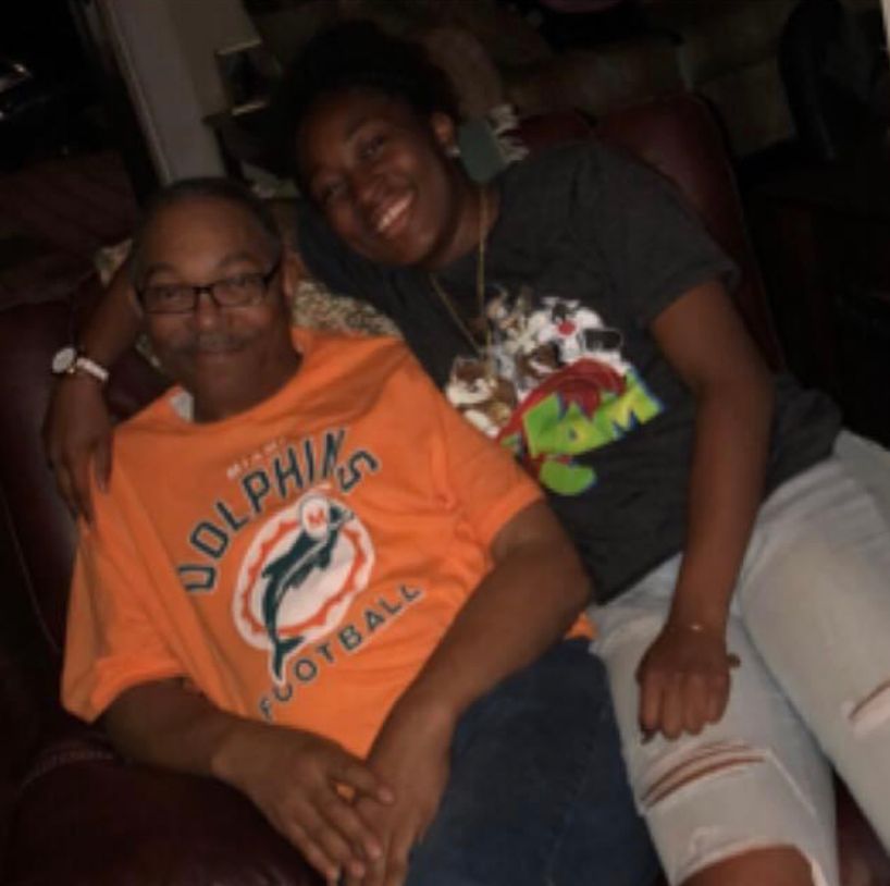 Two people smiling and relaxing together on a couch, one wearing a Miami Dolphins jersey.