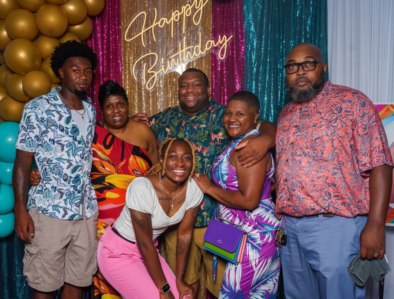Group of six people smiling together at a Happy Birthday celebration with balloon decor.