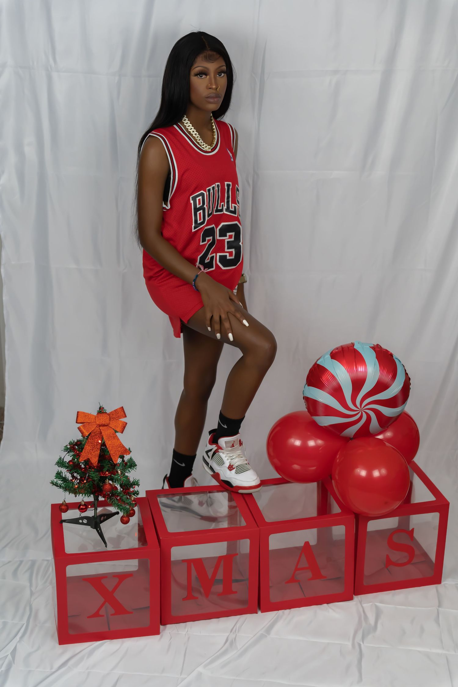 Woman in Bulls 23 jersey poses with foot on XMAS boxes with red balloons and mini Christmas tree.