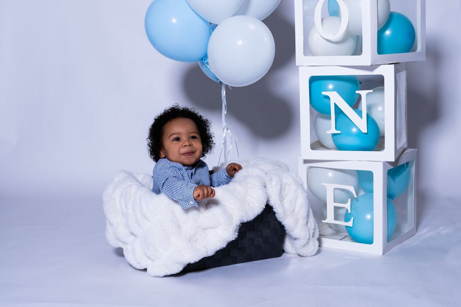 Baby's first birthday photo with blue balloons and decorative letter blocks spelling ONE.