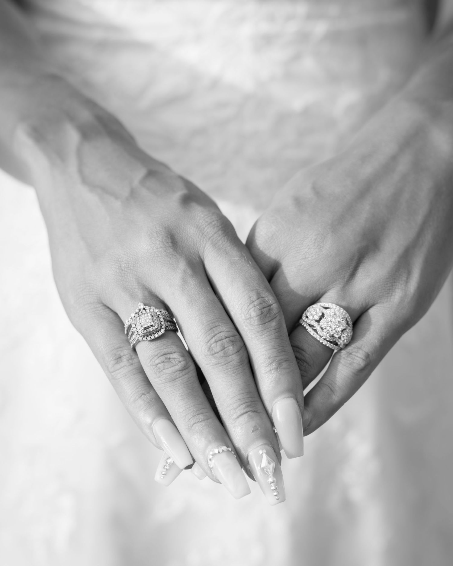 Close-up black and white photo of bride's hands showing two diamond wedding rings with elegant nail art.