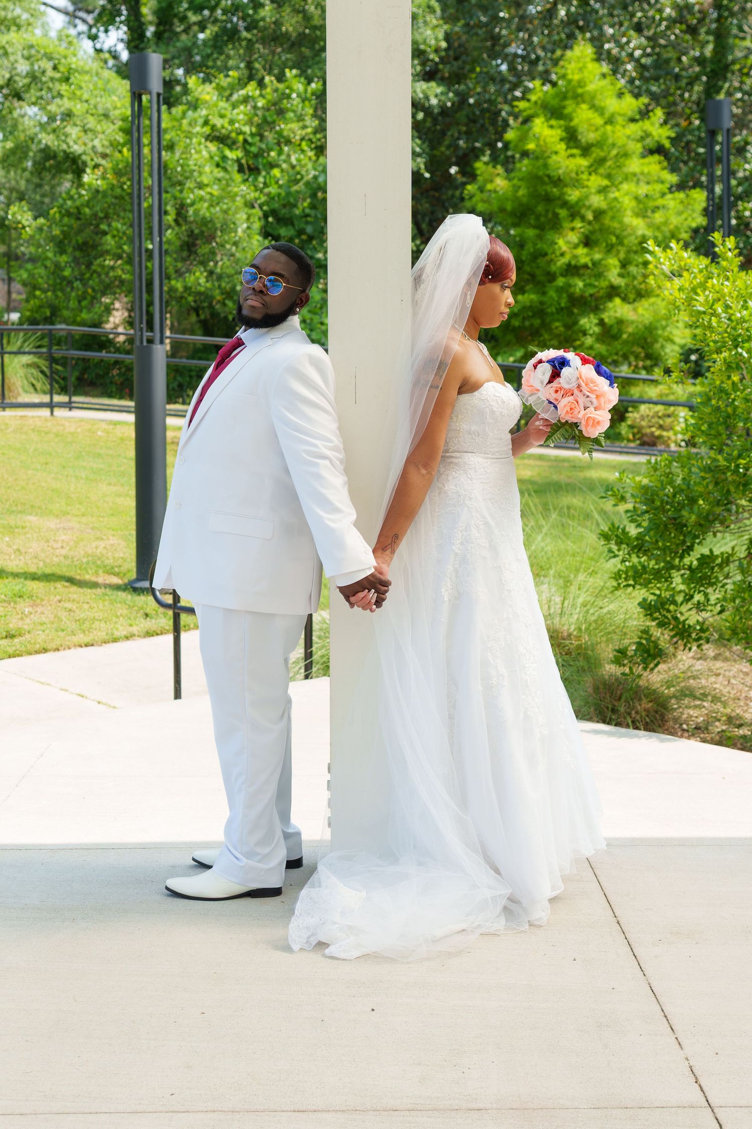 Bride and groom holding hands behind pillar in outdoor wedding photo.