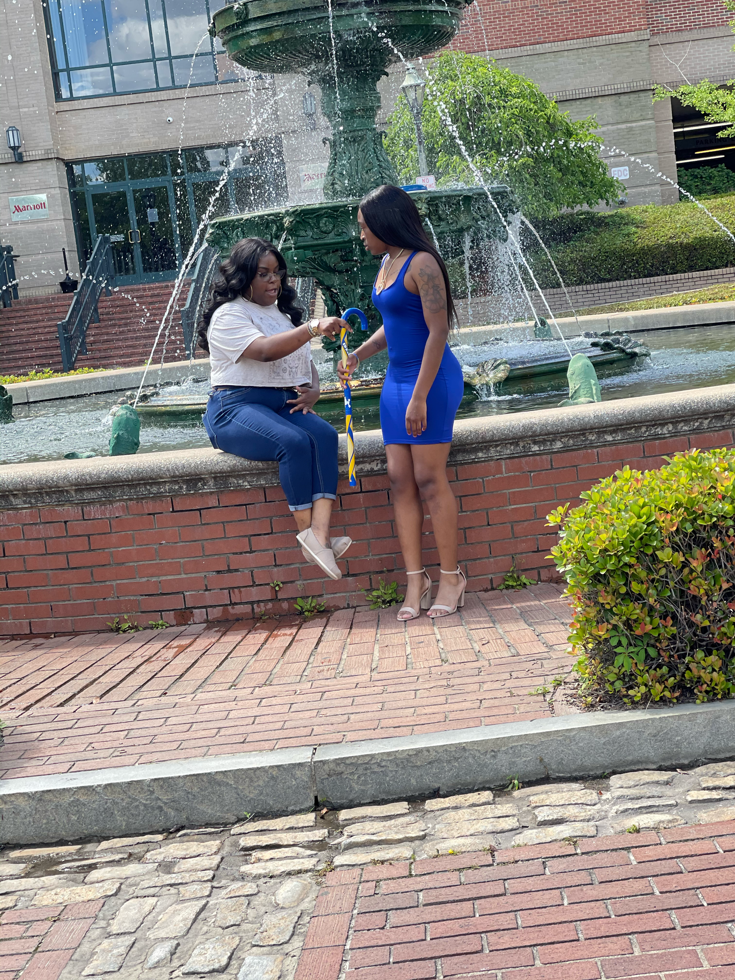 Two women conversing near a decorative brick fountain in an outdoor plaza.