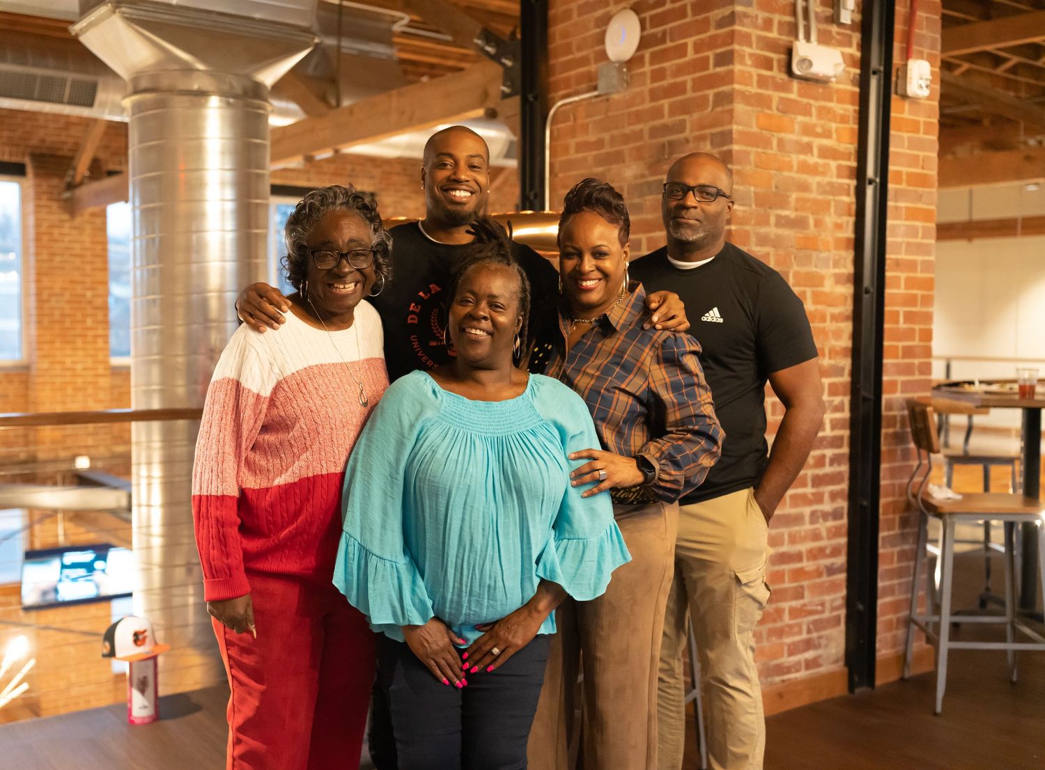 Group of five people smiling together inside a brick-walled venue.