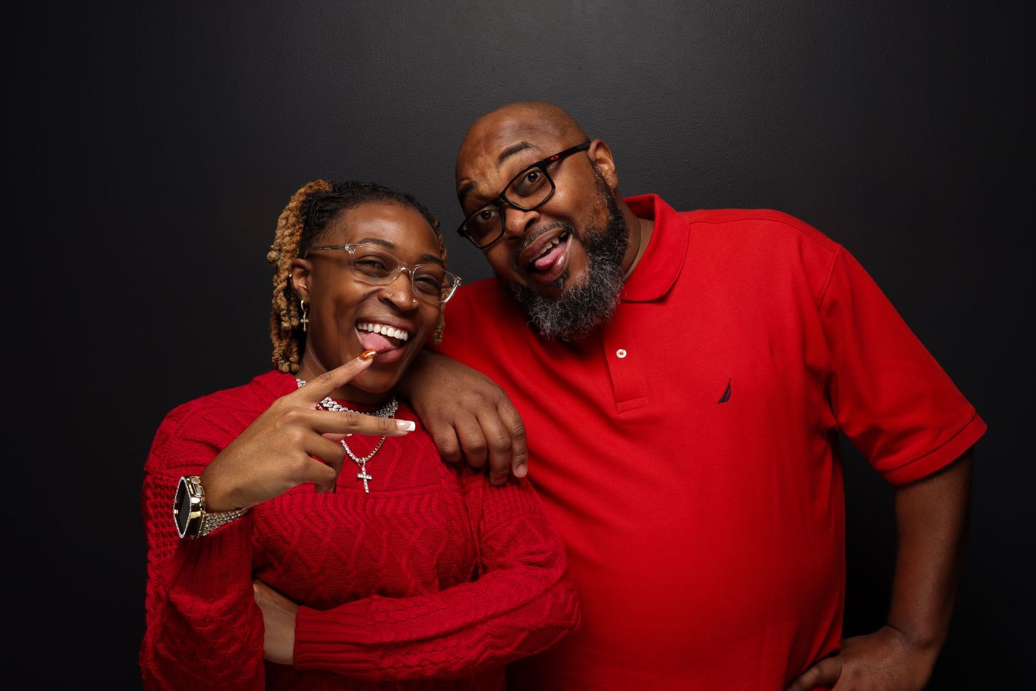 Smiling couple in matching red outfits posing together against a dark background.