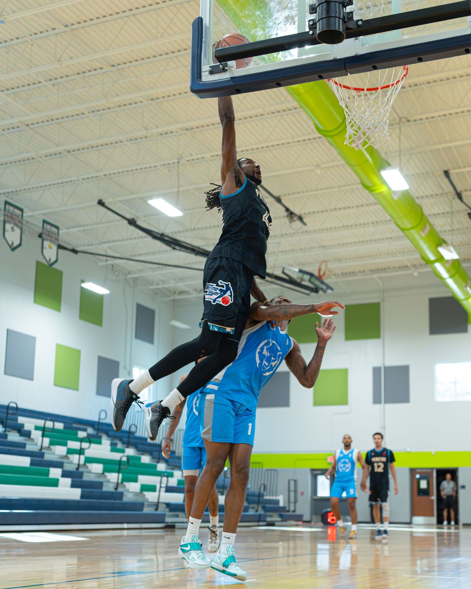 Basketball player performing a dramatic slam dunk over defenders during an indoor game.