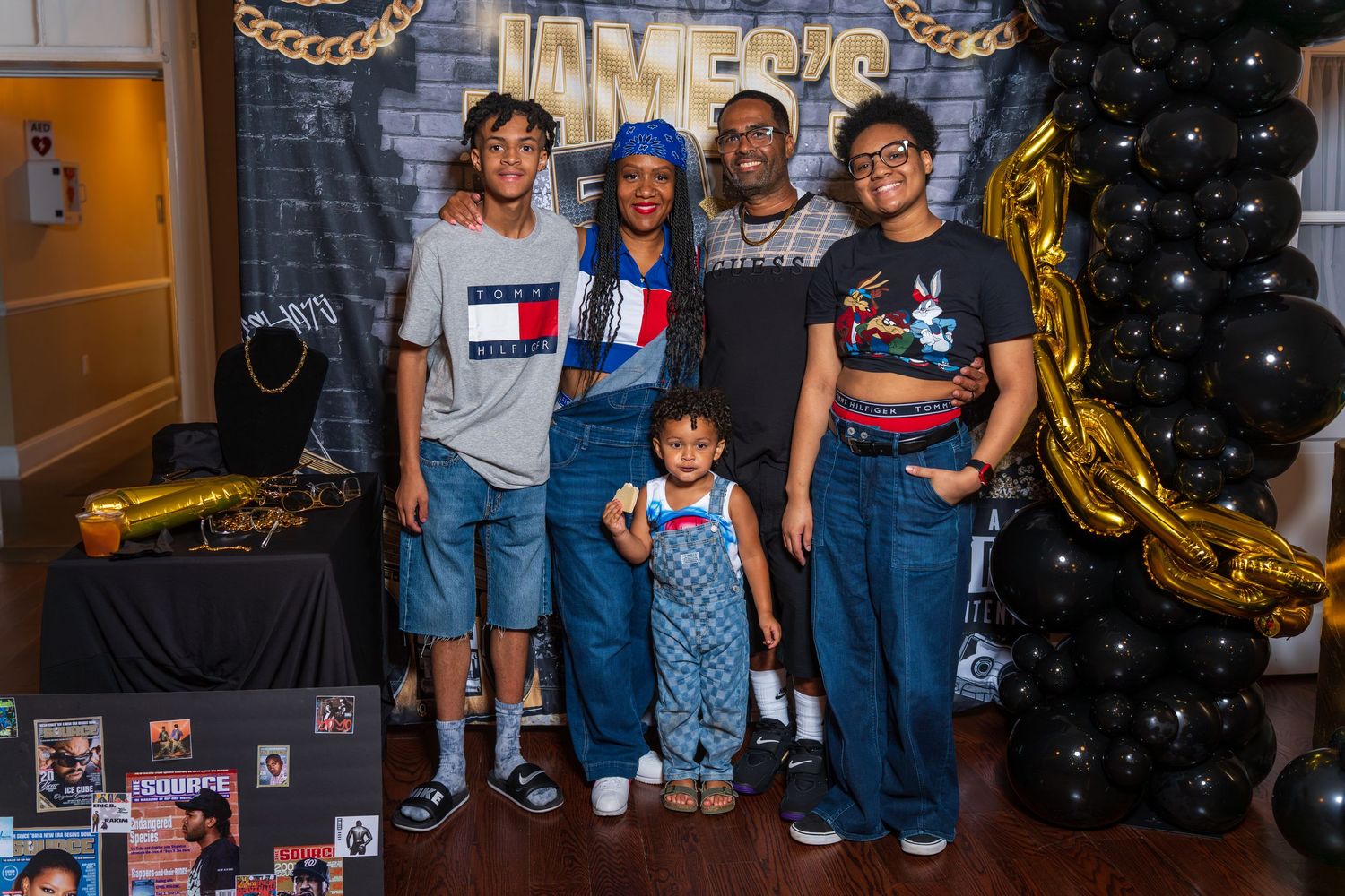 Family of five posing in front of a birthday party backdrop with gold balloons and decorations.