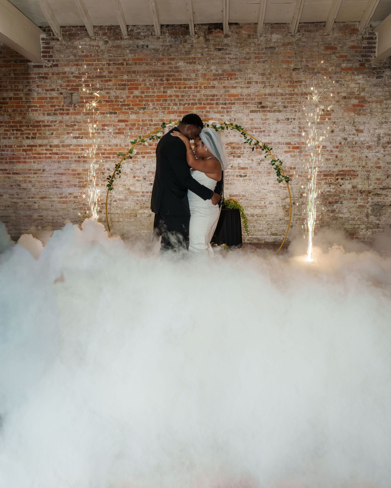 Bride and groom share first dance surrounded by dramatic fog machine clouds and sparkling fairy lights.