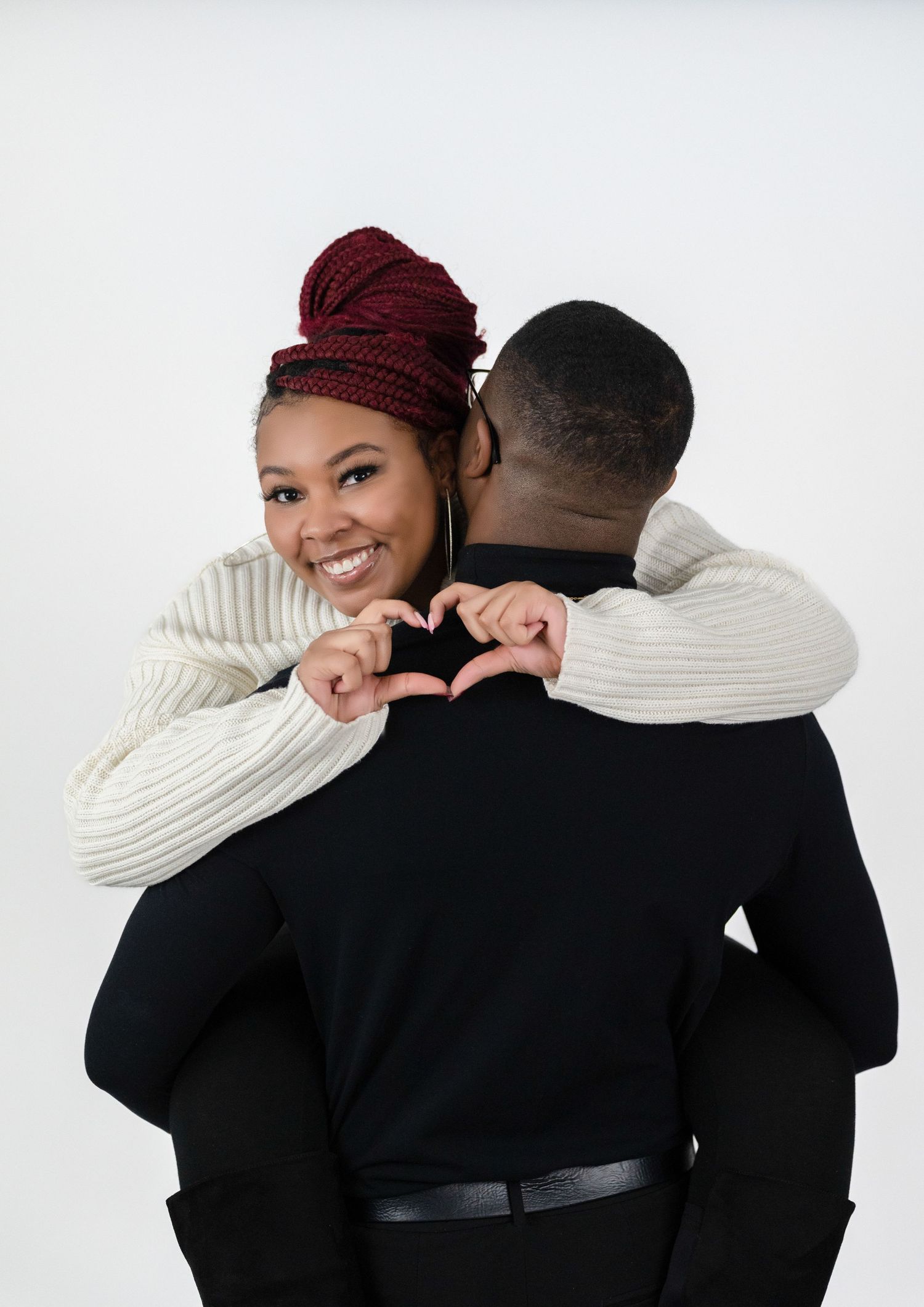 Smiling woman making a heart shape with her partner in a cozy sweater couples portrait.