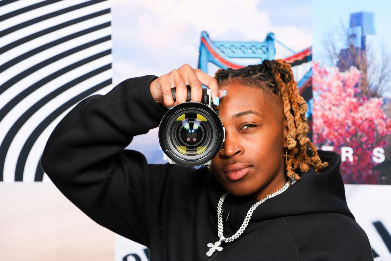 Young person holding a camera lens up to their eye in front of a colorful backdrop.