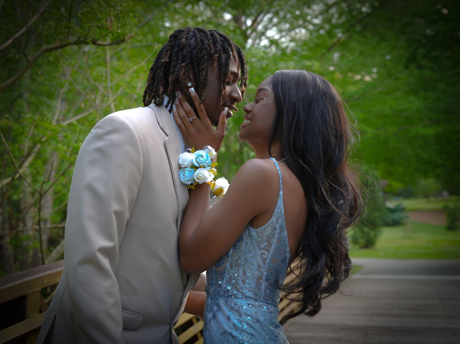 A young couple shares a romantic moment at prom, dressed in formal attire with corsages, on a wooden bridge.