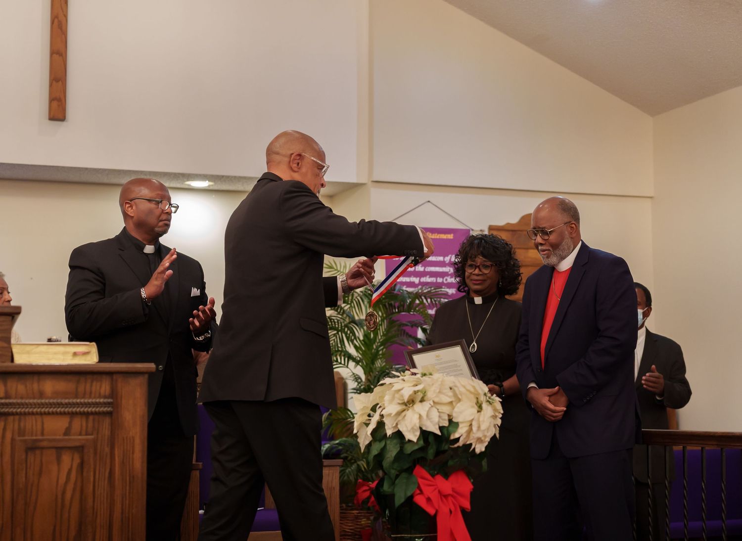 Men in formal attire shake hands during a church ceremony with floral decorations nearby.