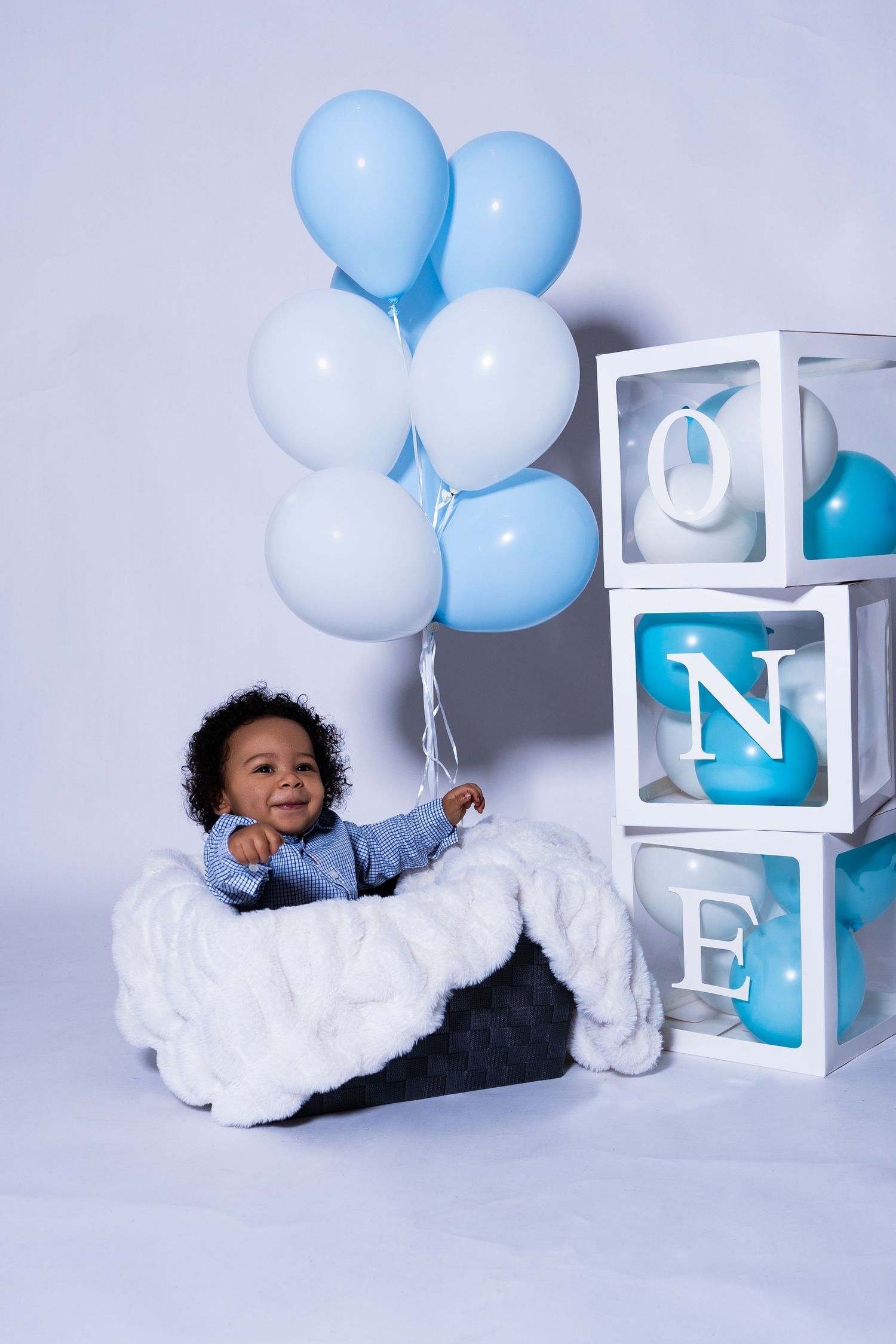 Happy baby boy sitting with blue balloons next to ONE birthday blocks decoration.