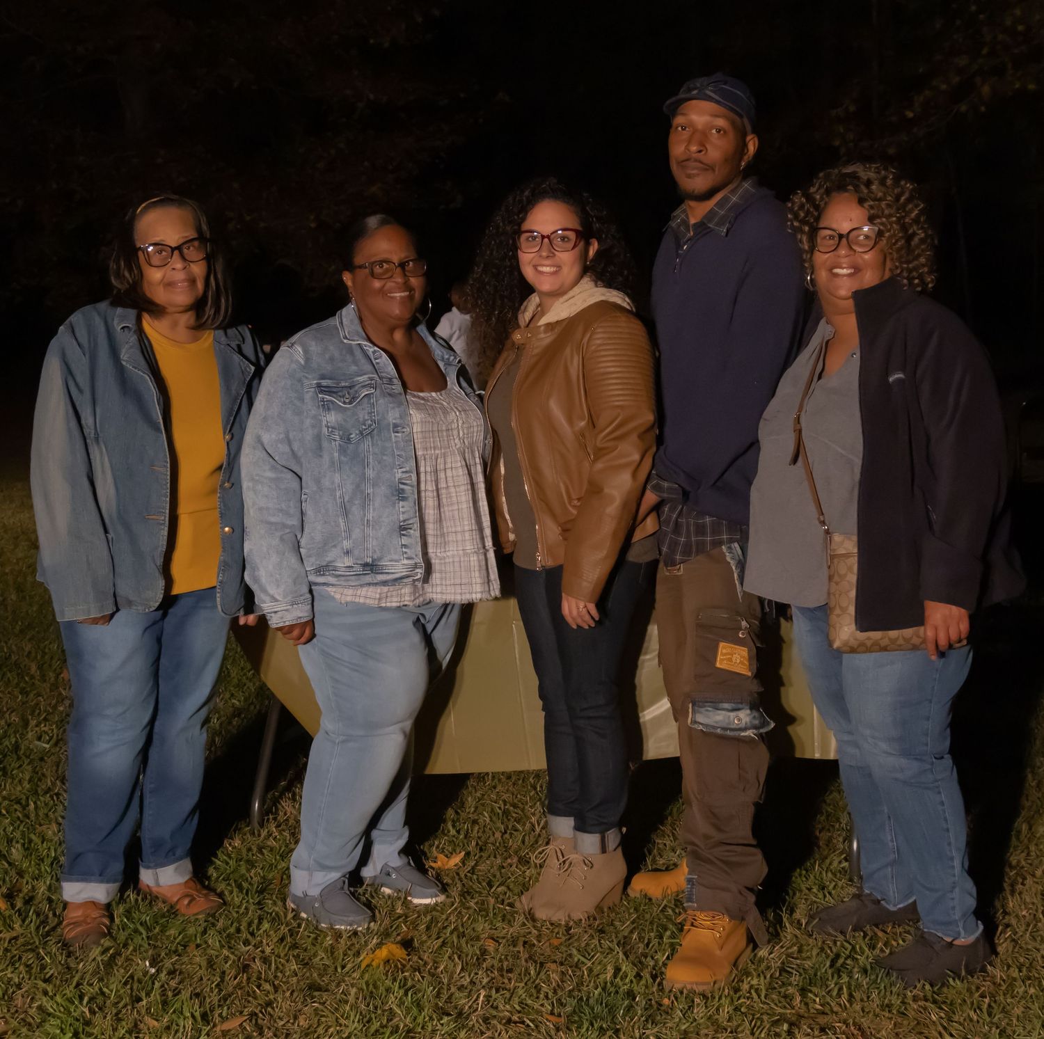 Five adults posing together outdoors at night near a tent in a grassy backyard setting.