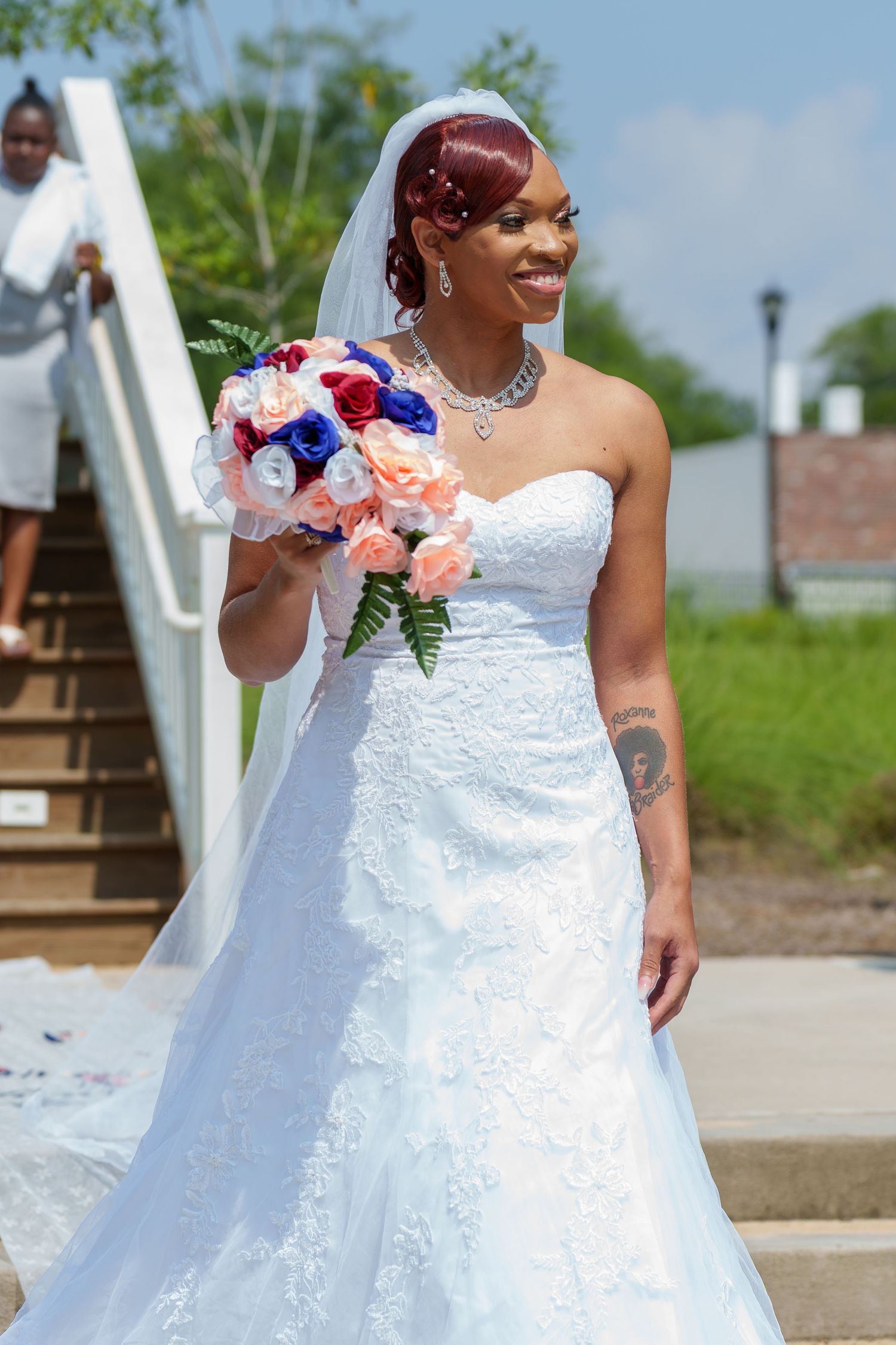 Smiling bride in white lace gown holding colorful bouquet of pink, red, and blue flowers.