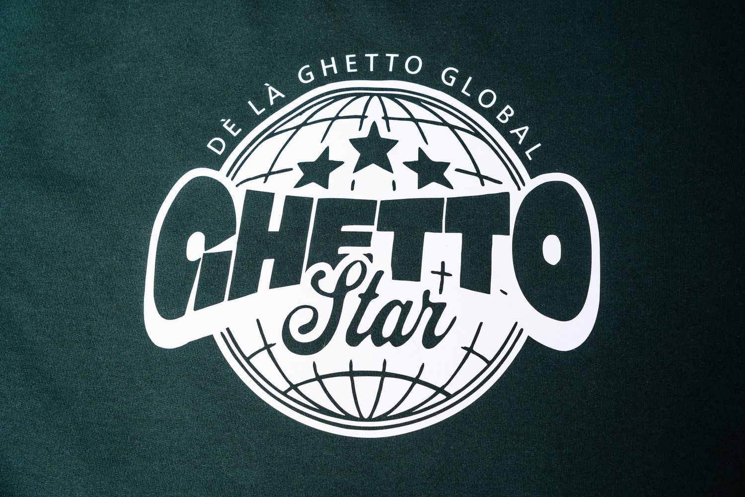 Close-up of De La Ghetto Global Ghetto Star logo on dark green fabric.