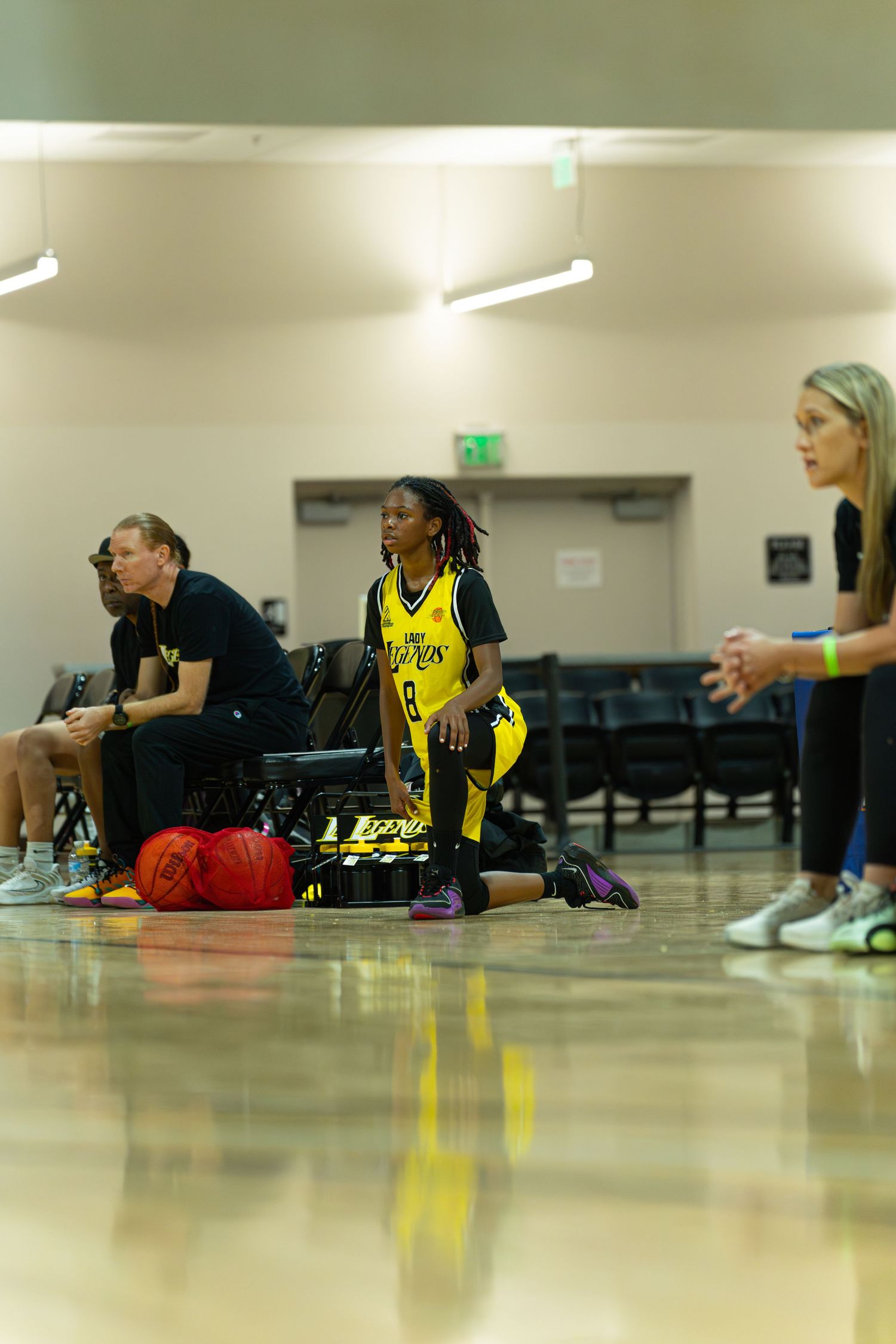 Female basketball player in yellow jersey kneeling courtside during a game in an indoor gymnasium.