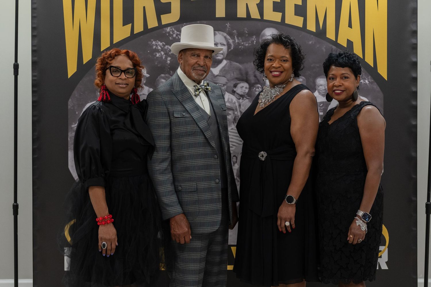 Four people posing in front of Wilks-Freeman banner, dressed in formal black attire.