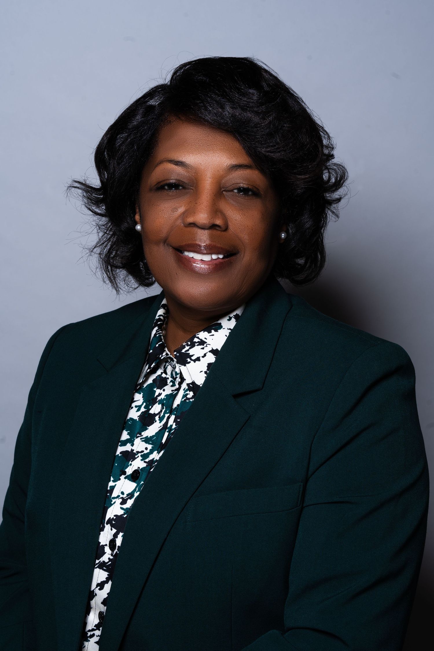 Smiling professional Black woman in green blazer and floral blouse portrait photo.