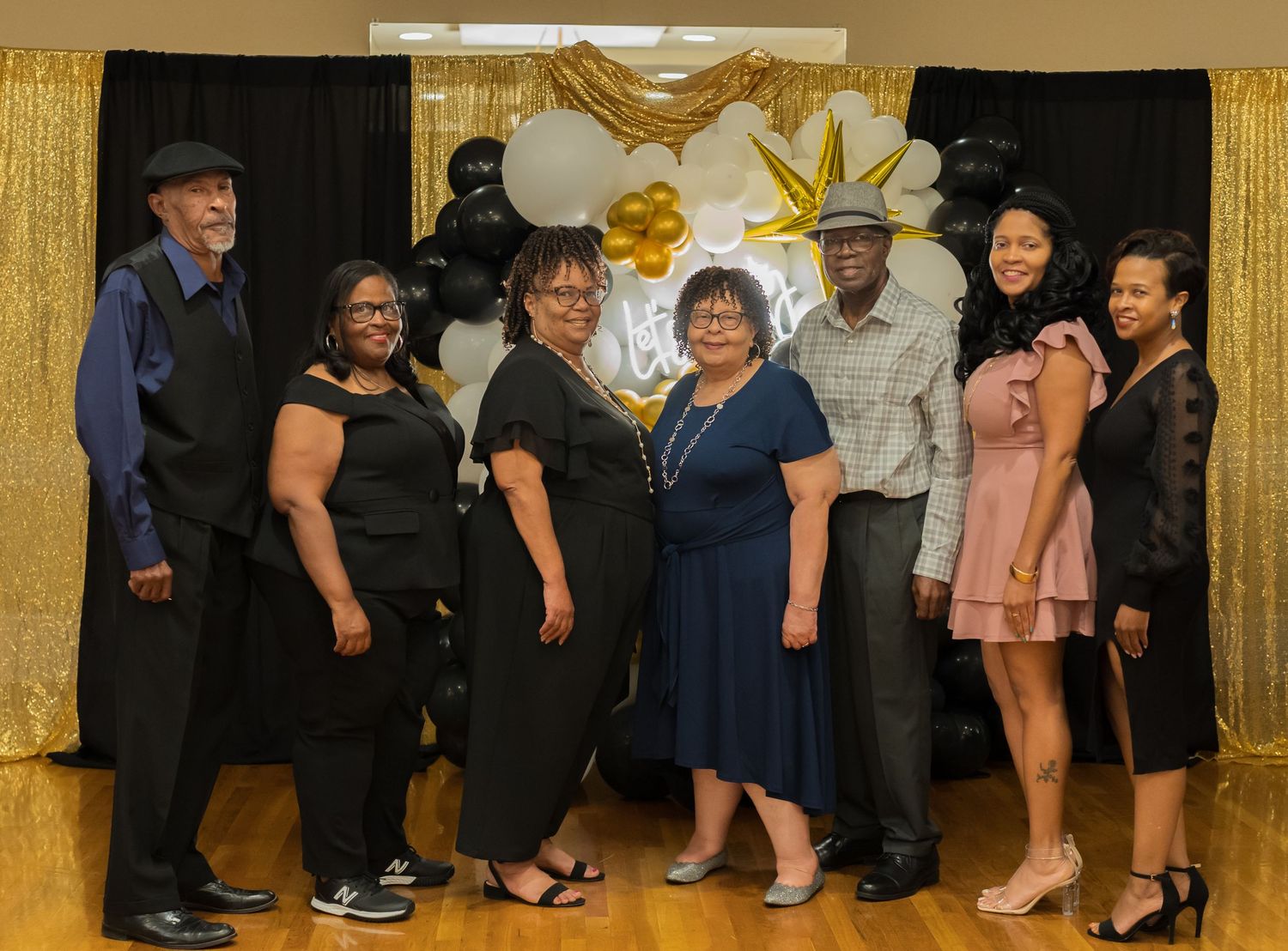Seven people posing together at a formal event with gold and black balloon decorations.