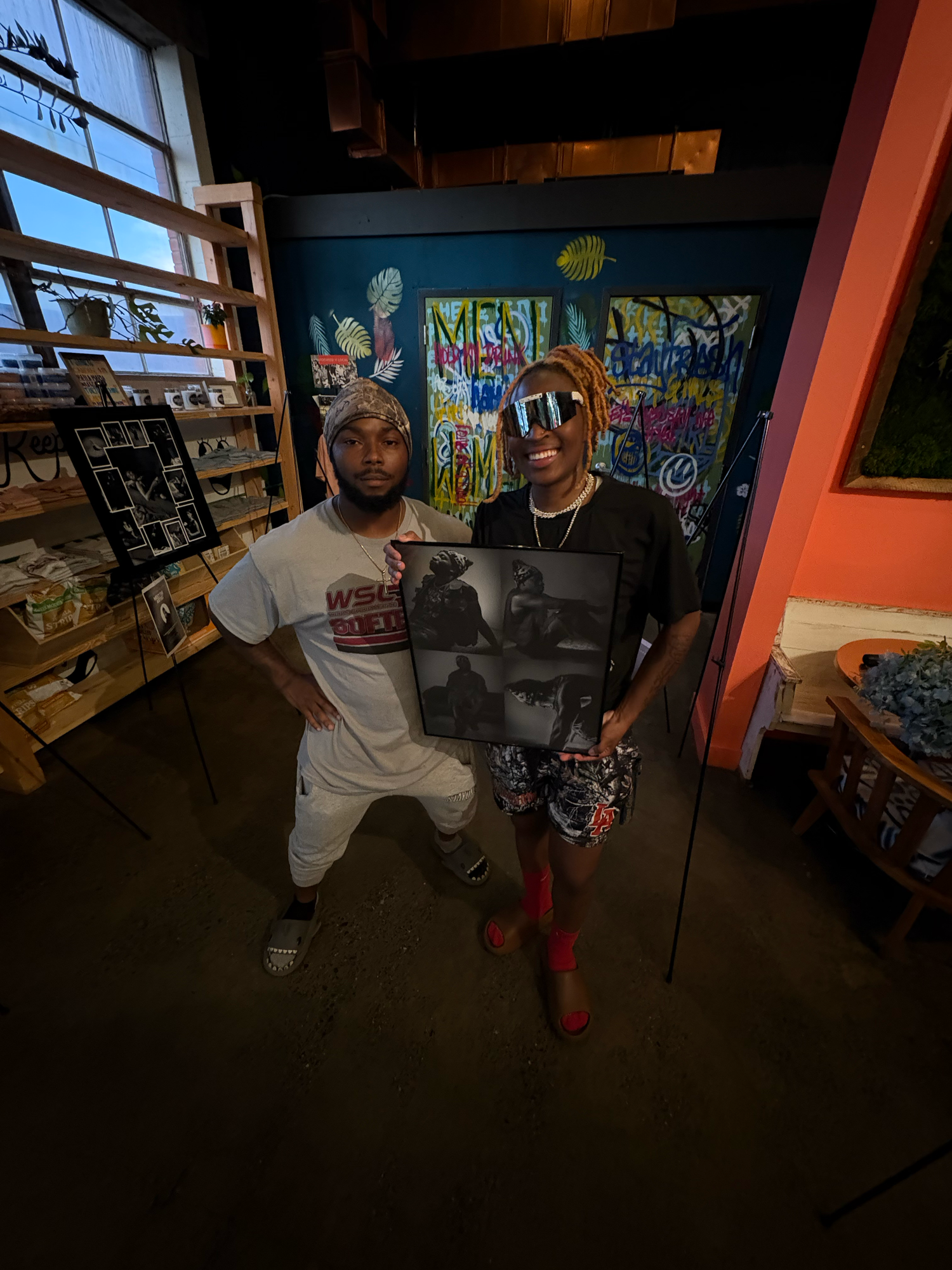 Two men posing indoors holding a framed black and white photo in an art shop.