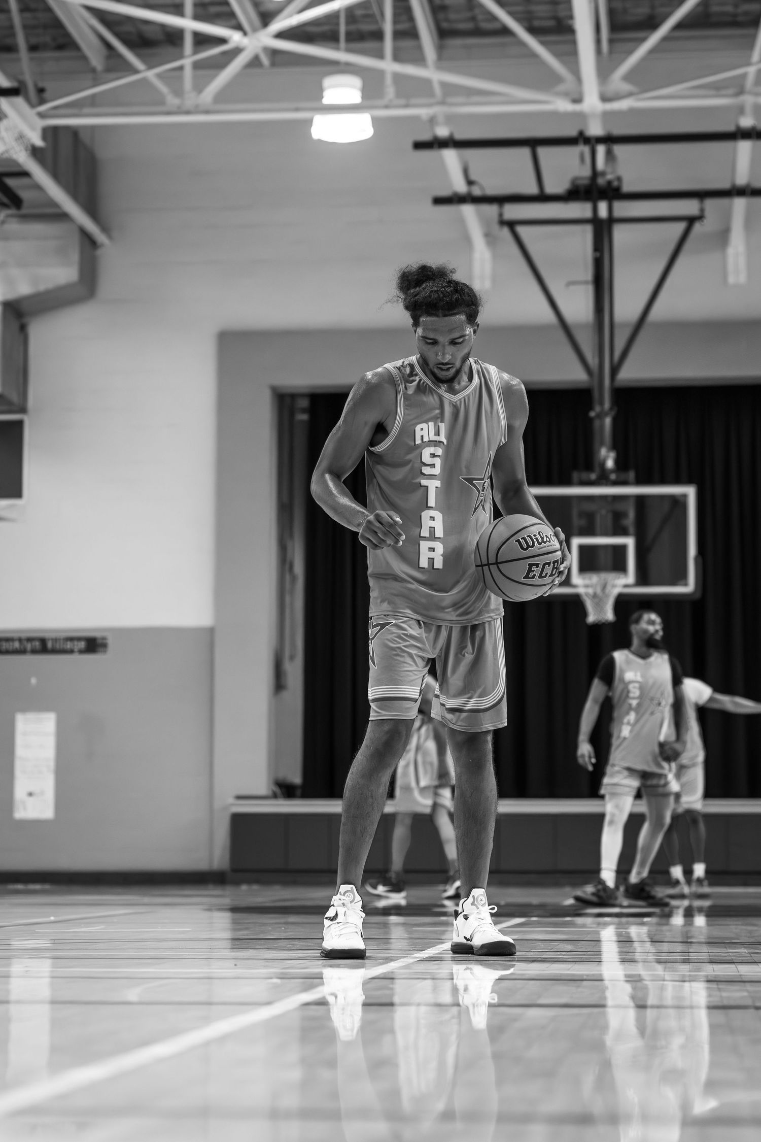 Black and white photo of All-Star basketball player dribbling ball on reflective indoor court.