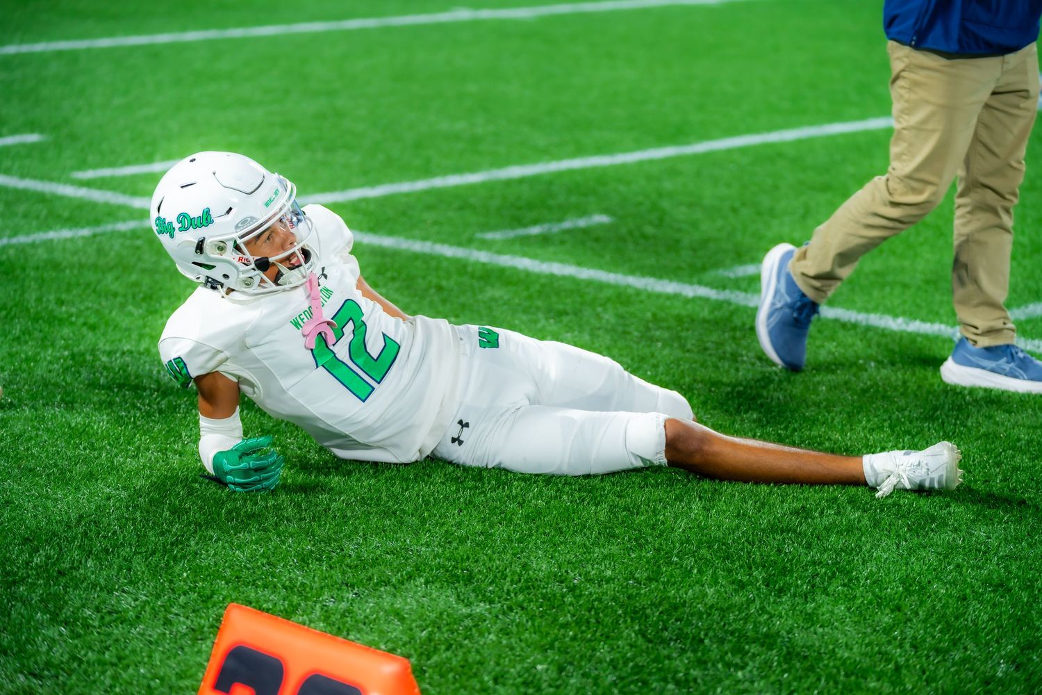 Football player in green uniform number 12 lies on turf after play during game.