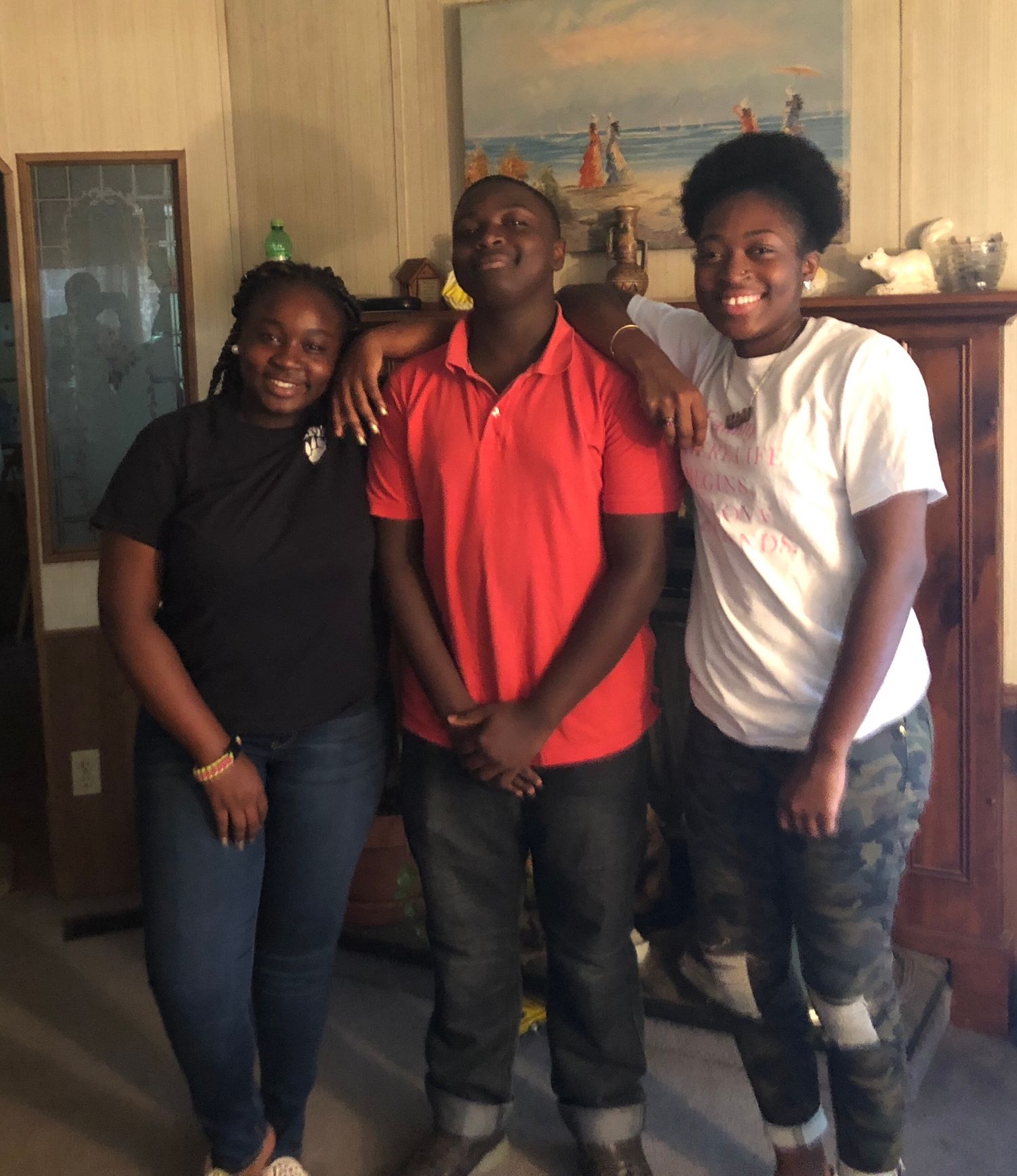 Three young people smiling and posing together inside a home living room.