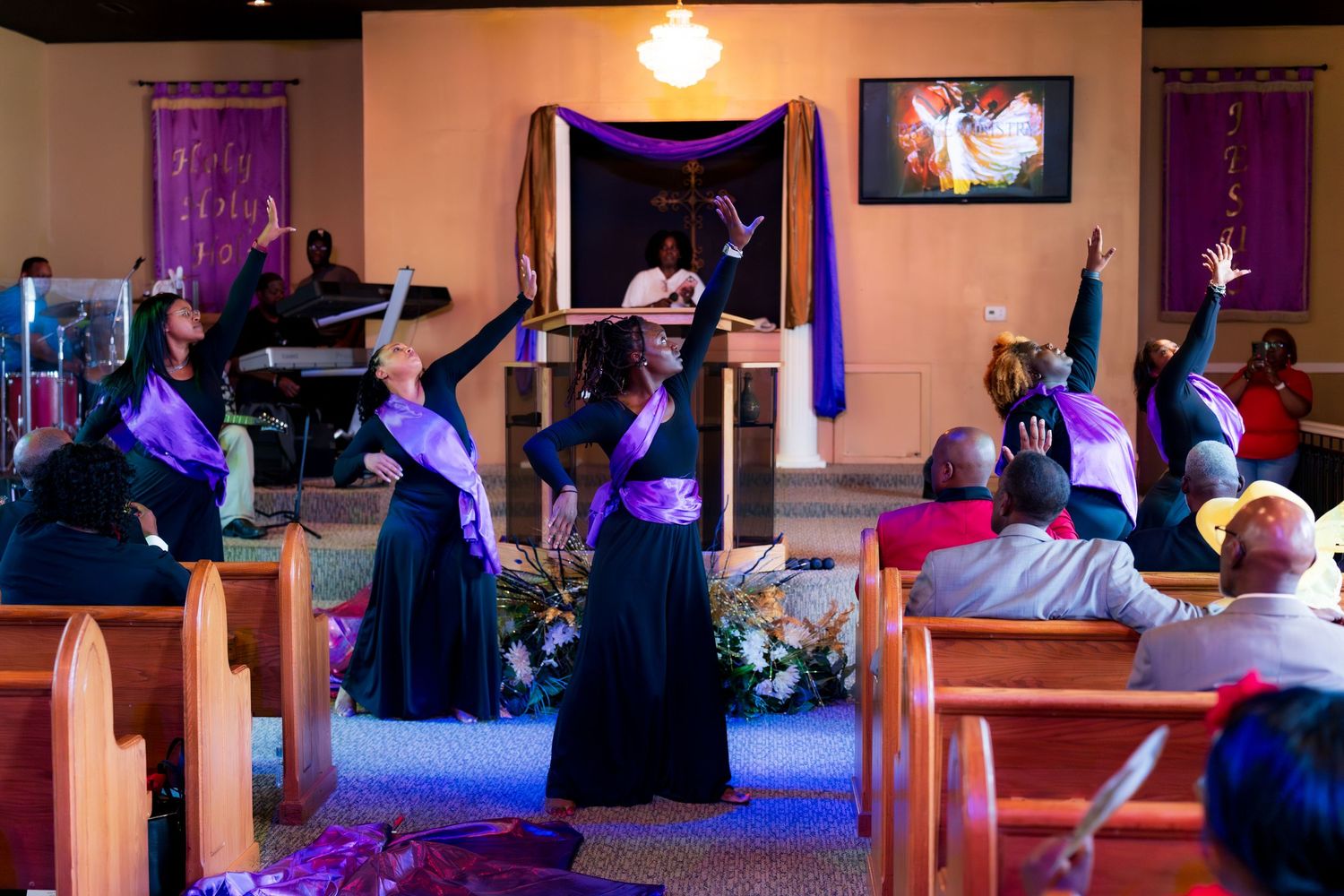 Liturgical dance team in purple and black performing gracefully before congregation in decorated church.