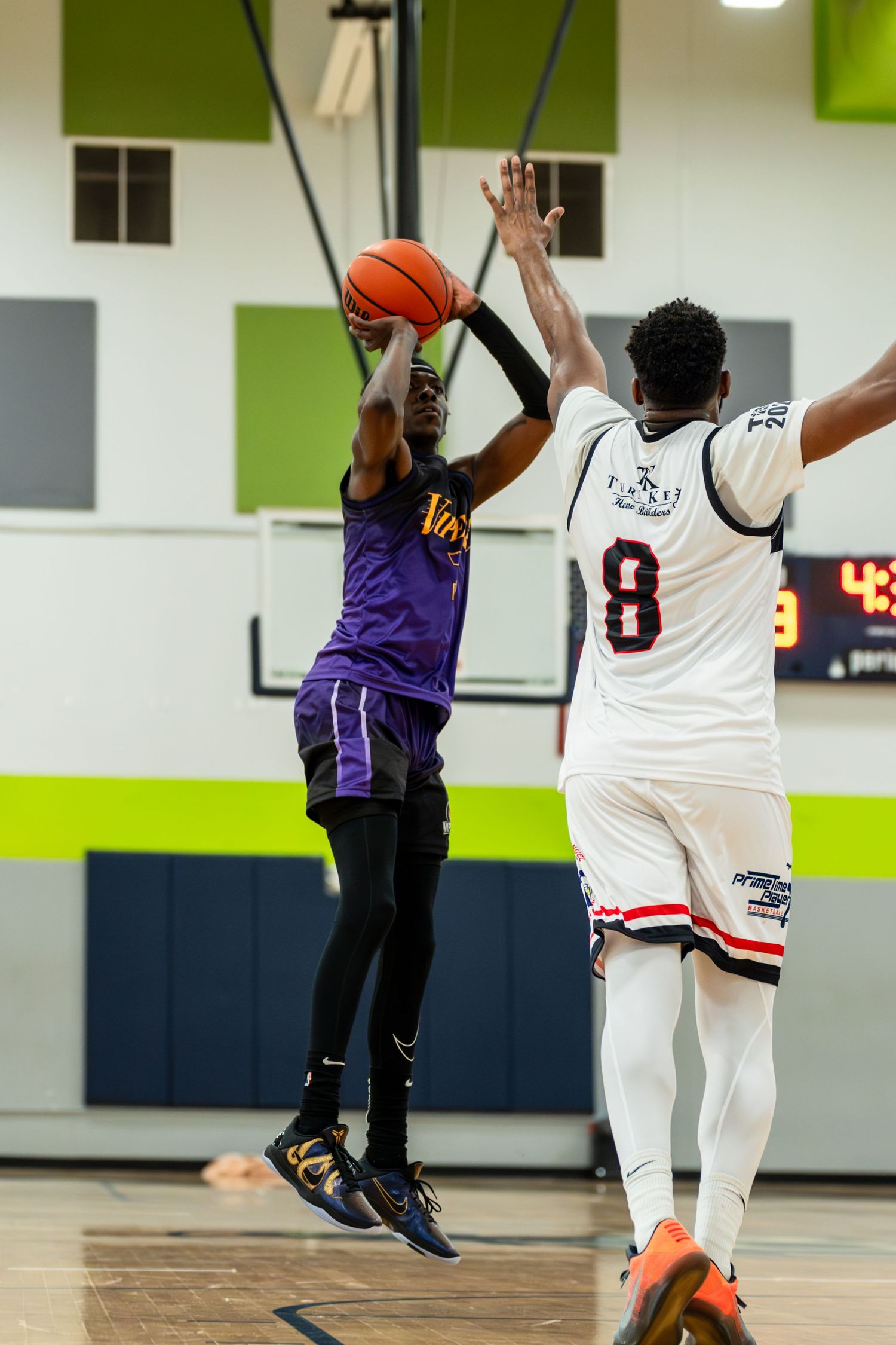 Basketball player in purple jersey jumping to shoot over a defender wearing number 8.