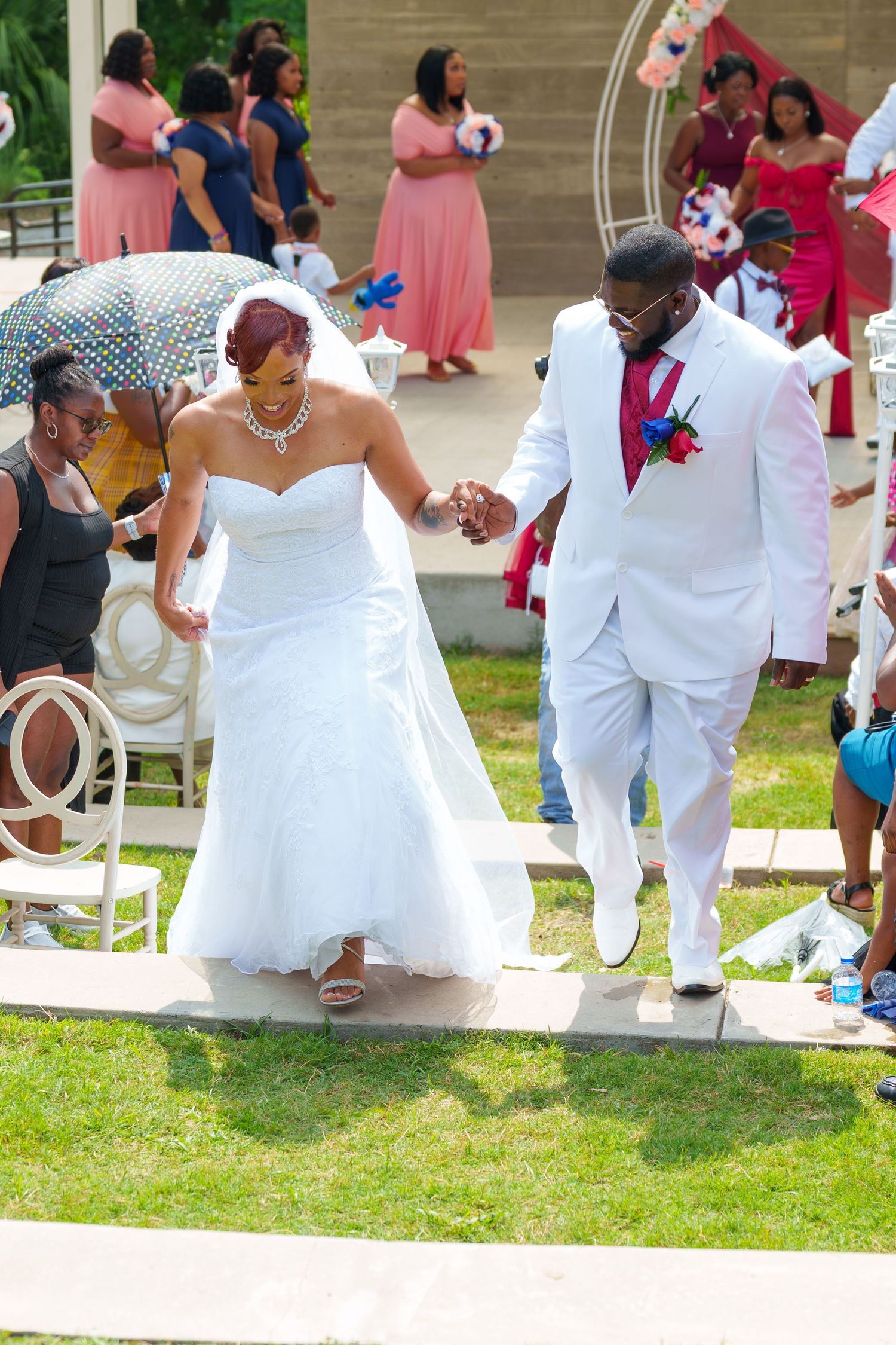 Joyful newlyweds holding hands walking back down the aisle after outdoor wedding ceremony.