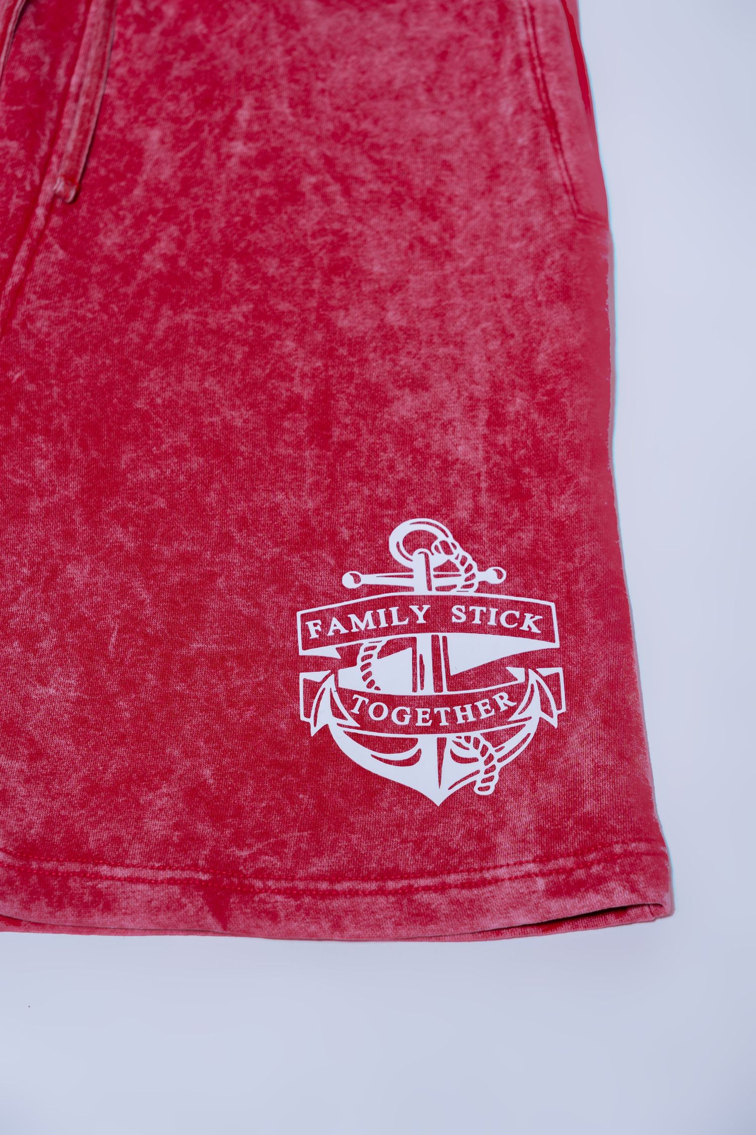 Close-up of red acid wash shorts with white Family Stick Together anchor logo.