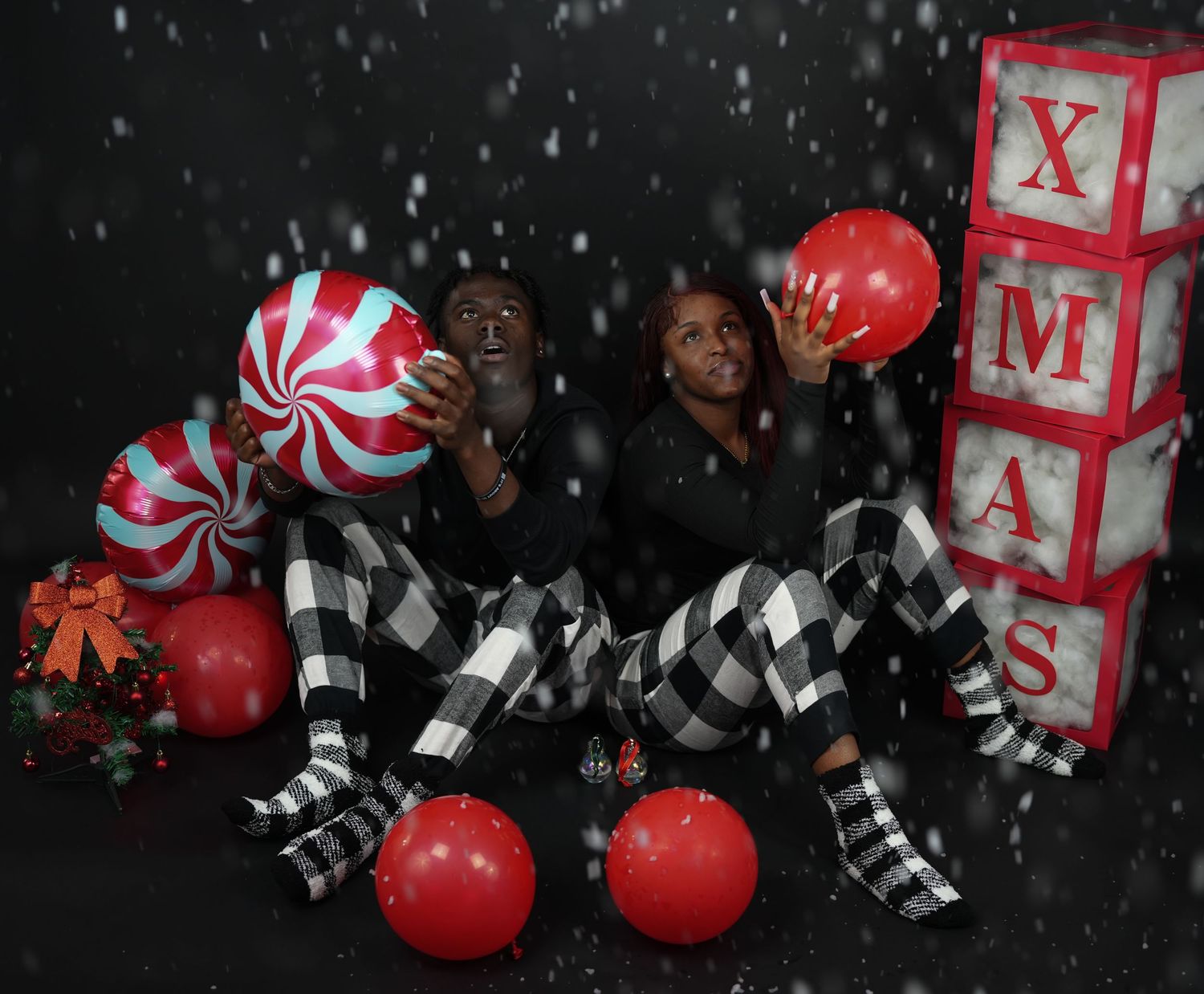 Couple in matching plaid pajamas posing with Christmas decorations and balloons.
