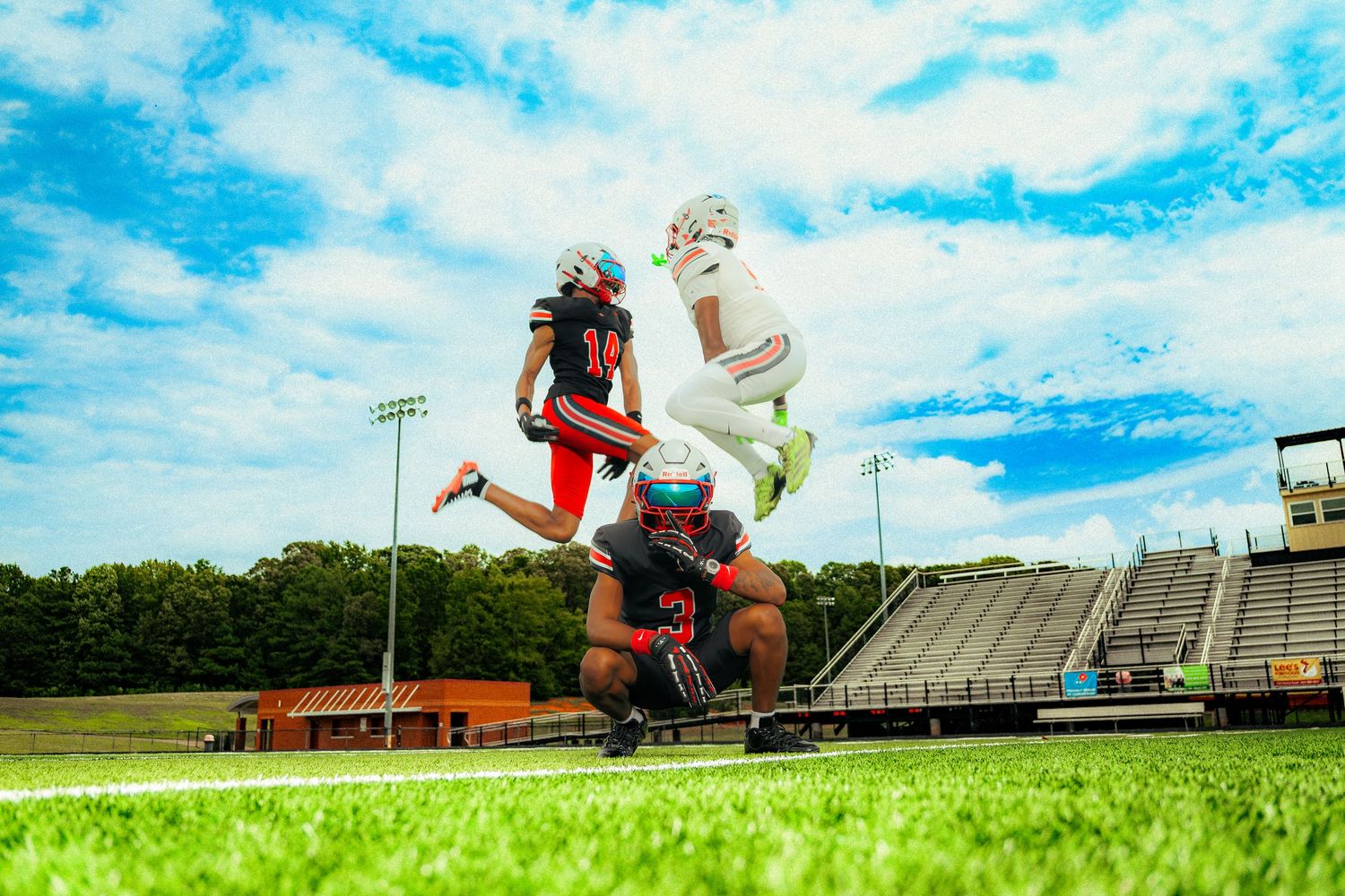 Football players in red and white uniforms practice on a bright green field under blue sky.