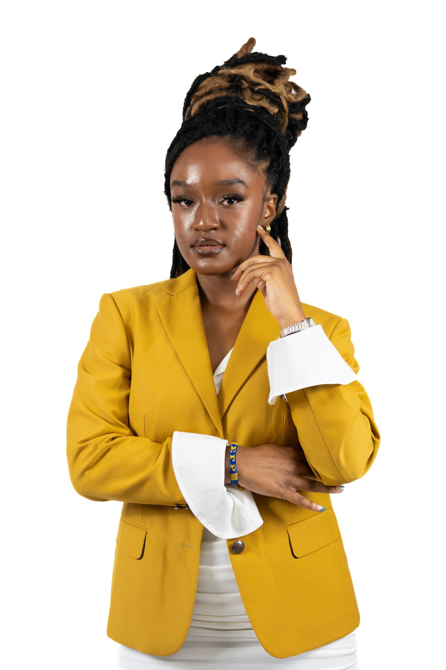 Confident woman with dreadlocks in yellow blazer posing against white background.