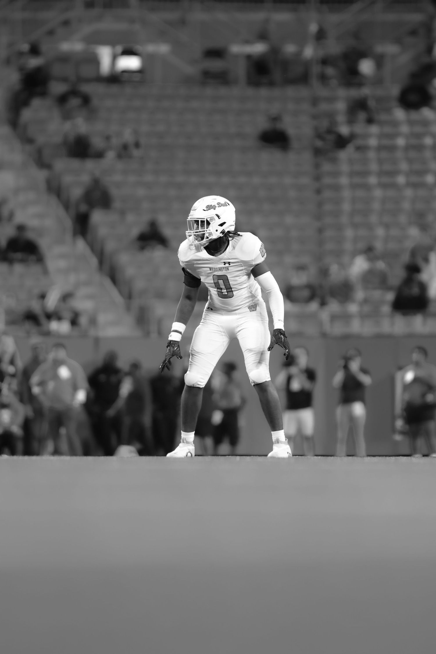 Black and white photo of football player in white uniform standing ready on stadium field.