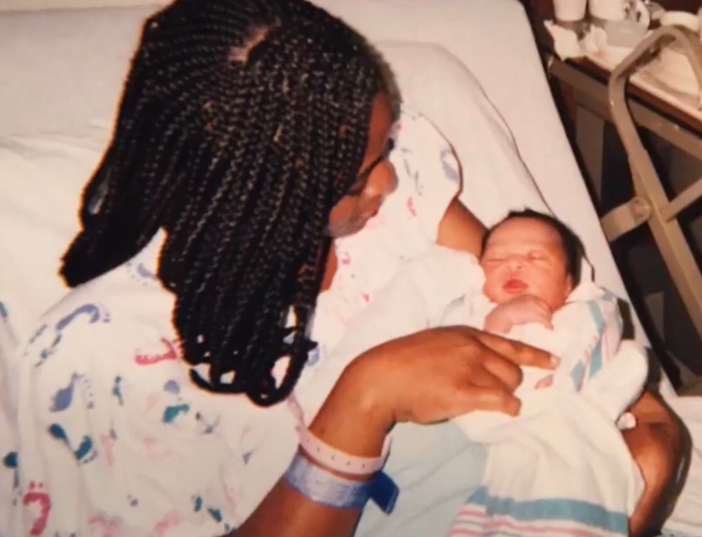 A mother in a hospital gown tenderly holds her newborn baby while sitting in a hospital bed.