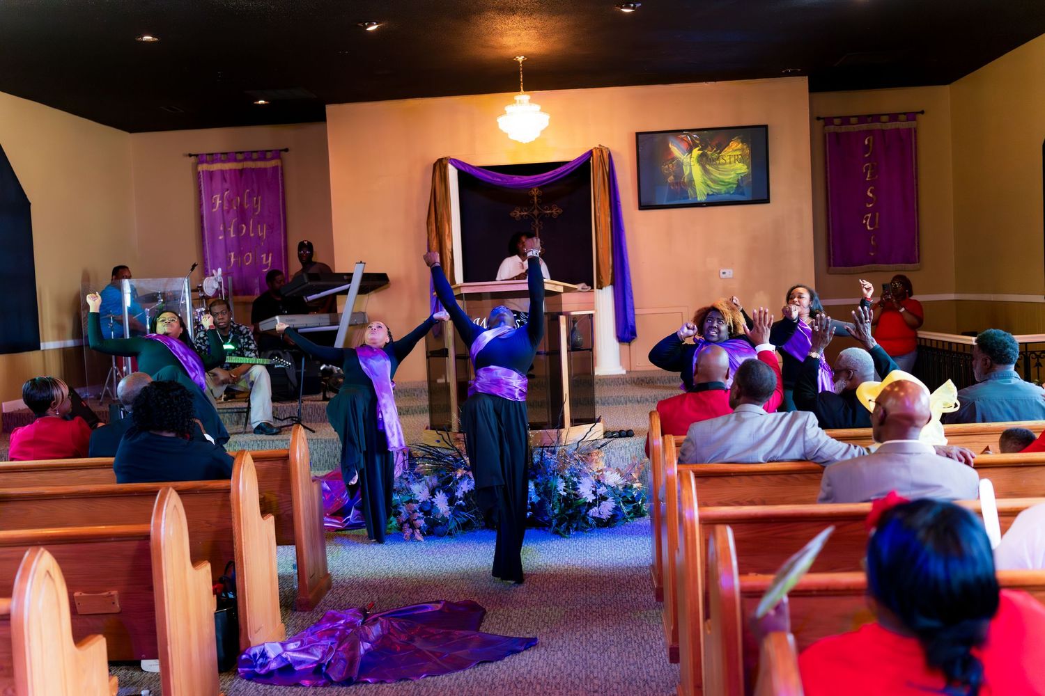 Performers in purple robes dance at the front of a decorated church during a worship service.