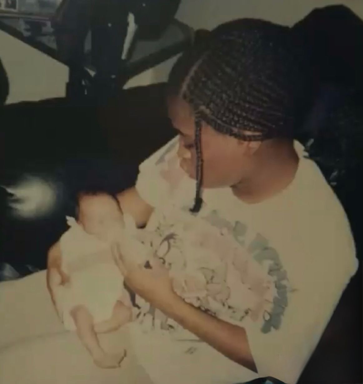 Young woman with braids tenderly holding and kissing a newborn baby outdoors.