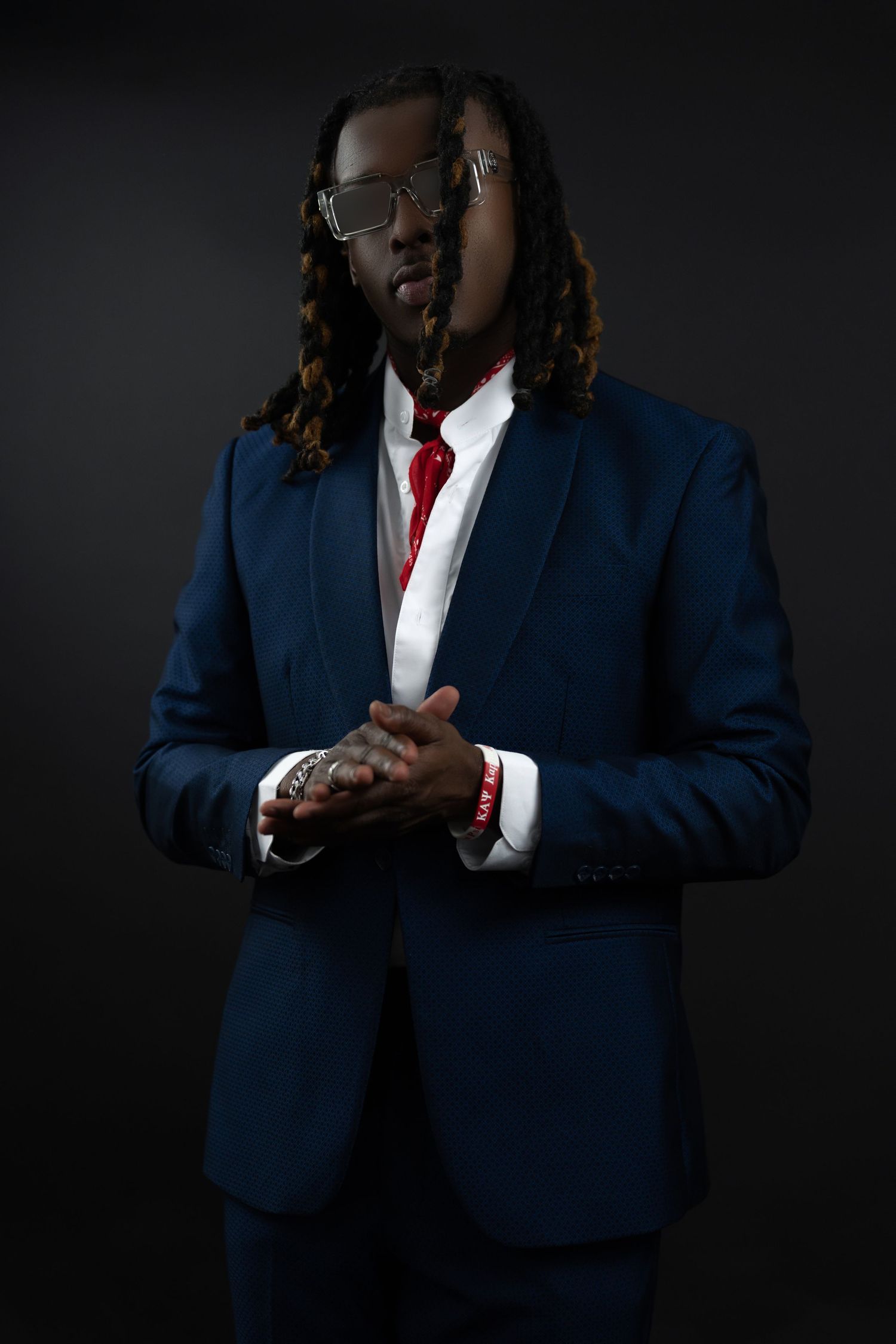 Stylish man in a navy blue suit with red tie and long dreadlocks posing in dark studio.