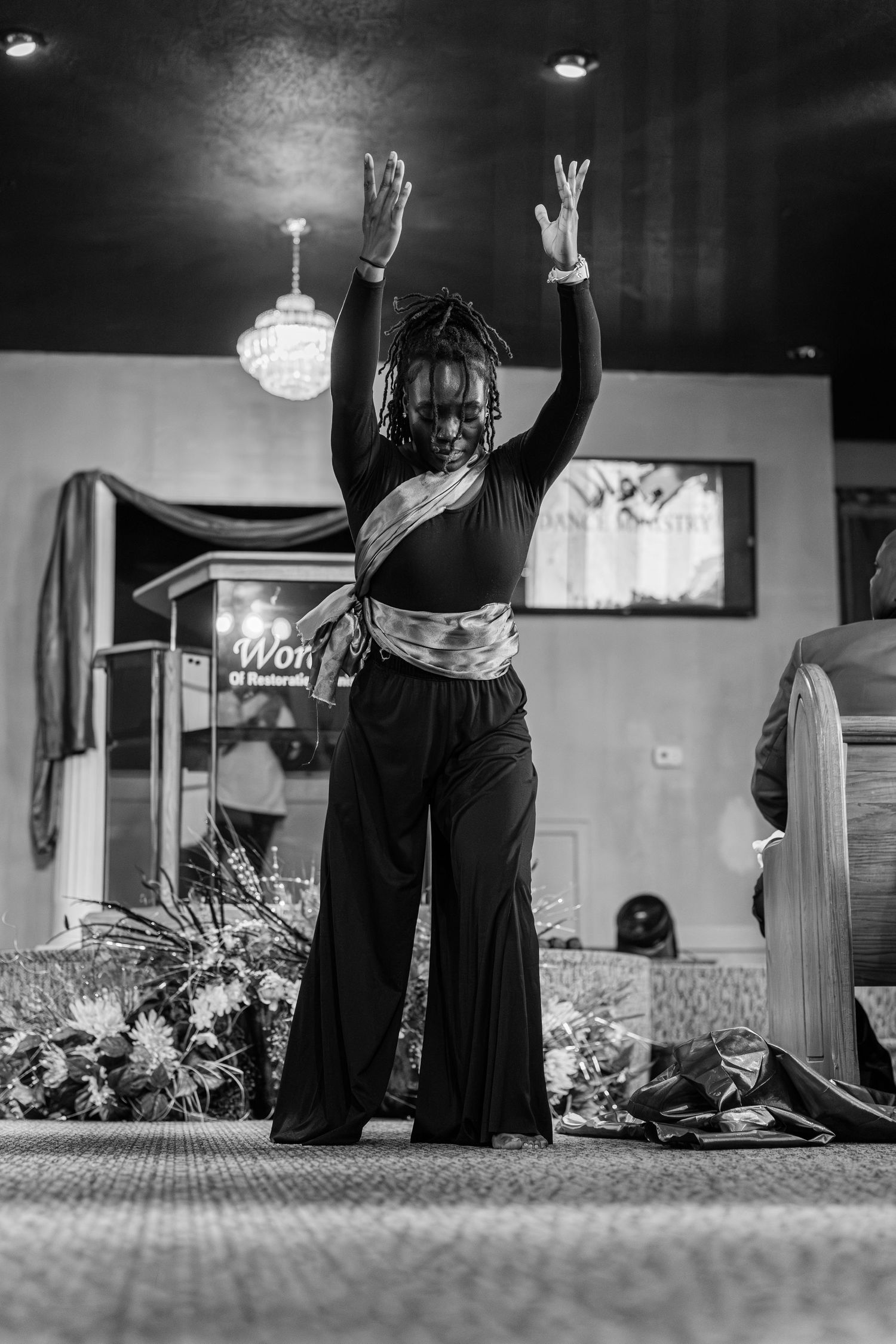 Black and white photo of woman with raised arms performing liturgical dance in church sanctuary.