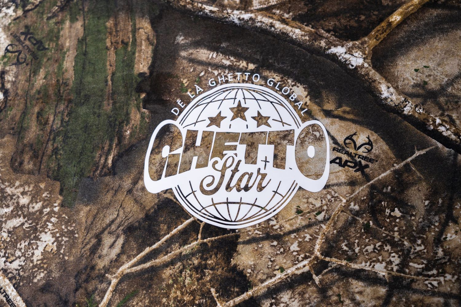 Close-up of Ghetto Star logo on camouflage fabric showing globe and stars design.