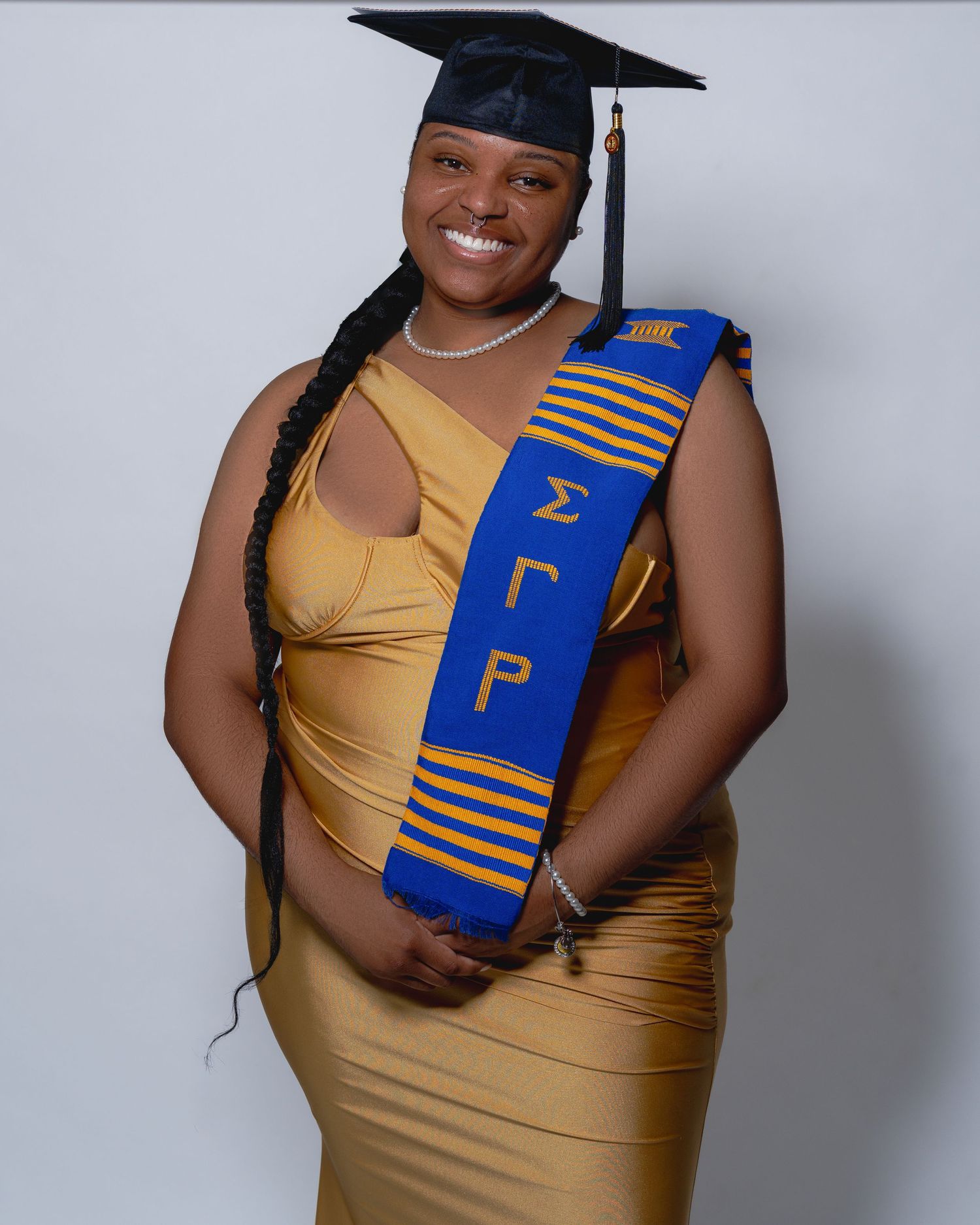 Smiling Black woman in gold dress wearing Sigma Gamma Rho blue and gold graduation stole and mortarboard cap.